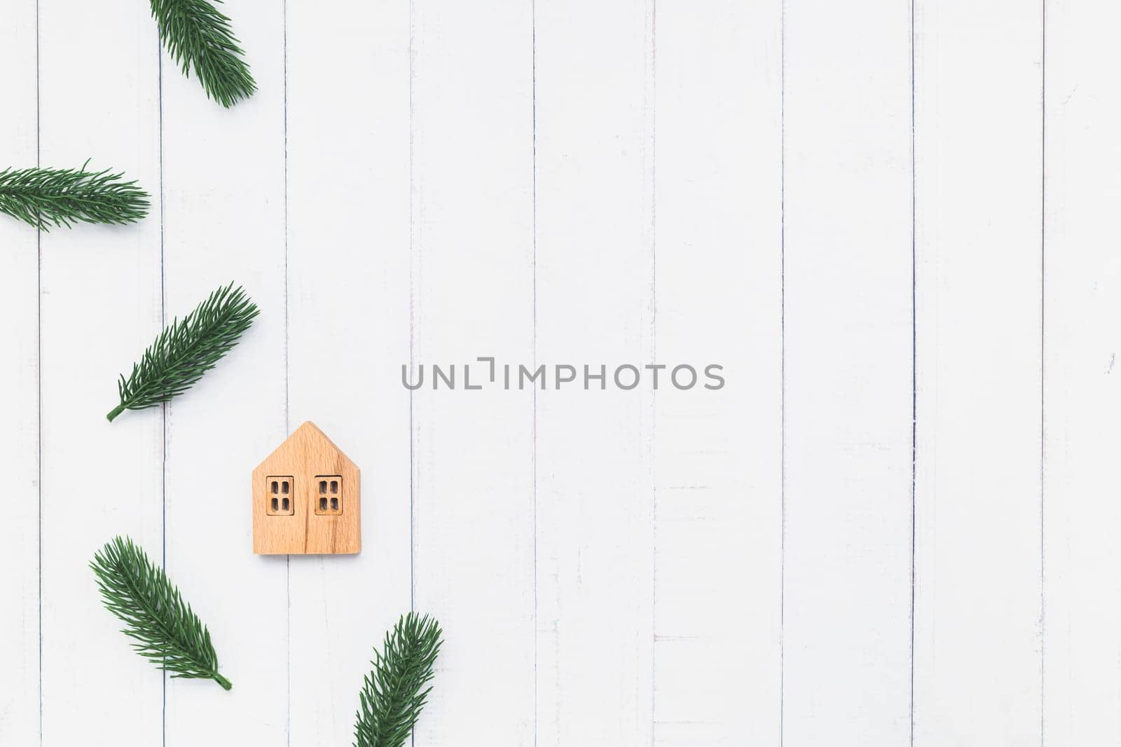 Flat lay of the wooden house model with fir tree branches on white table background for family and Christmas decoration concept