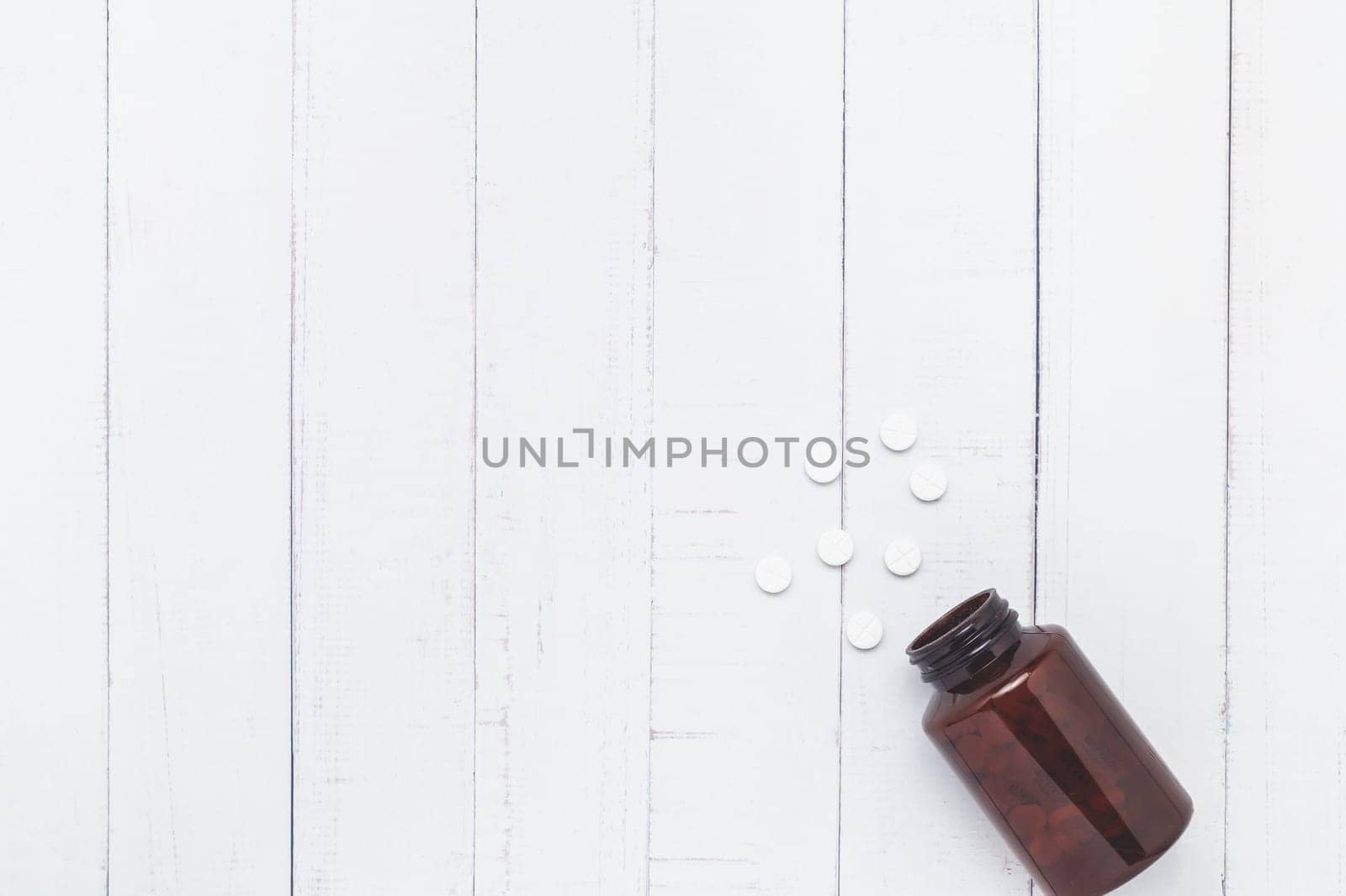 Flat lay of piles of pills were released from the brown bottle on white table background for medical and healthcare concept