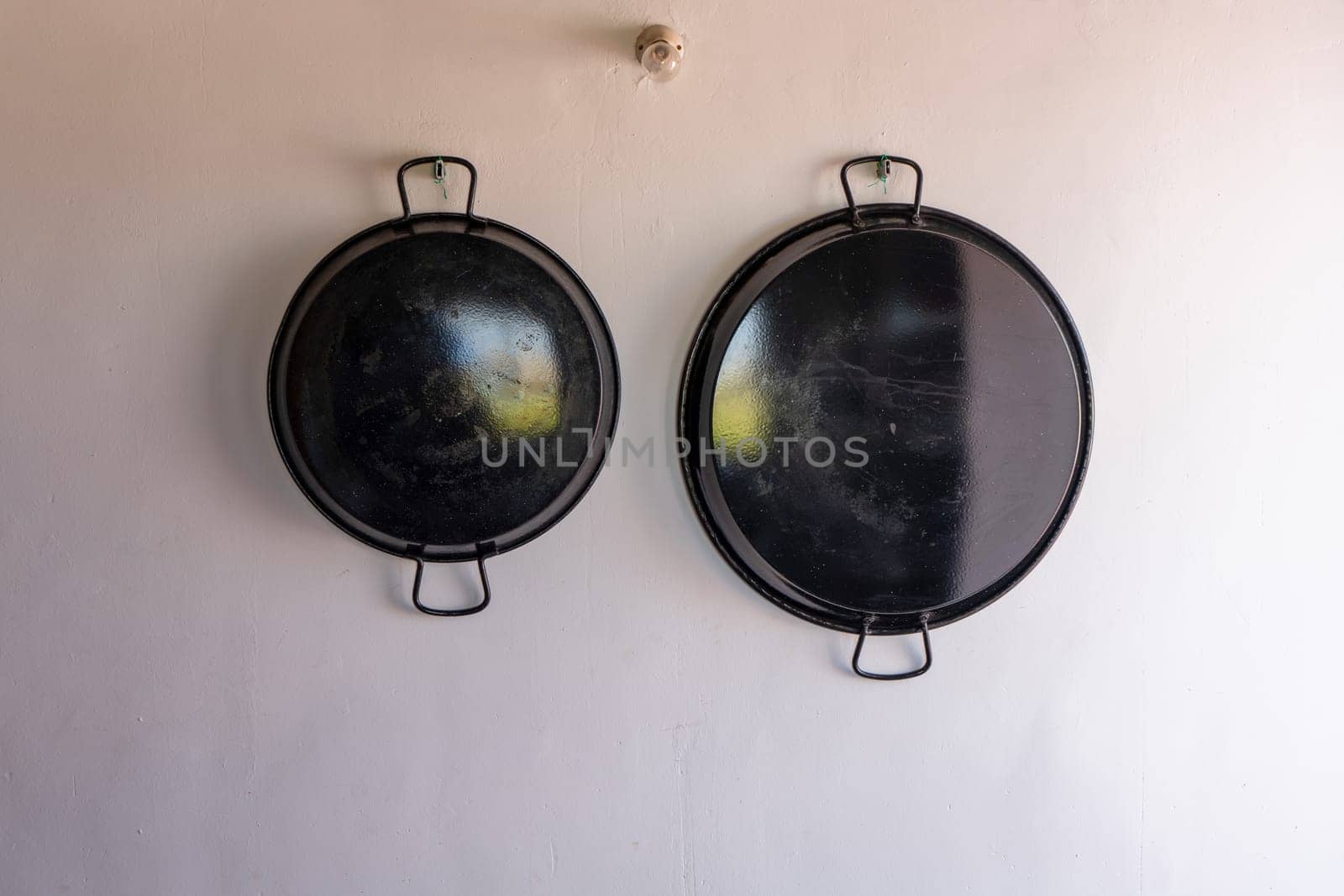 Paella pans hanging on the white wall, utensil for paellas, traditional Spanish food.
