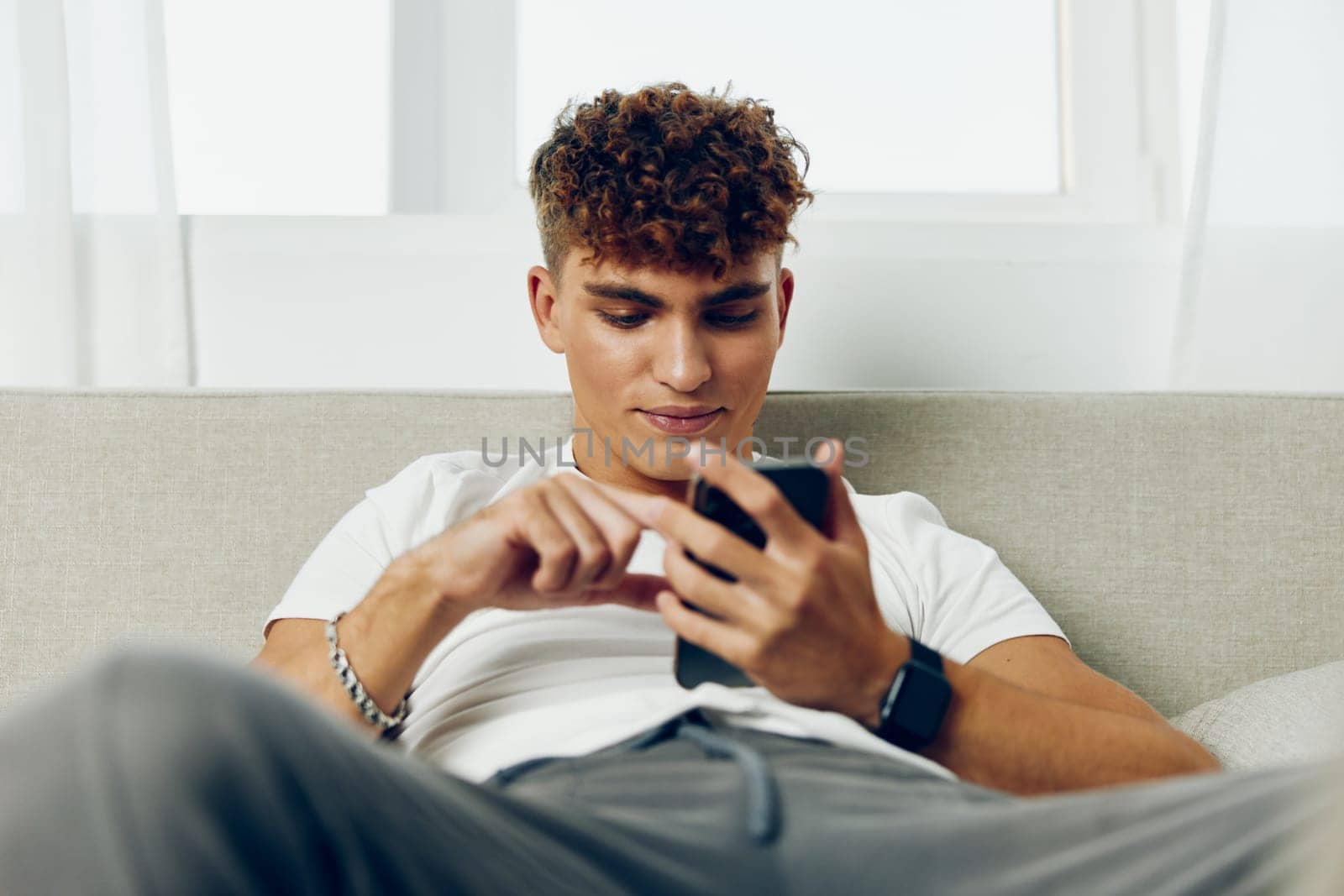 man interior teenager cell selfies cellphone message young sitting internet sofa by SHOTPRIME