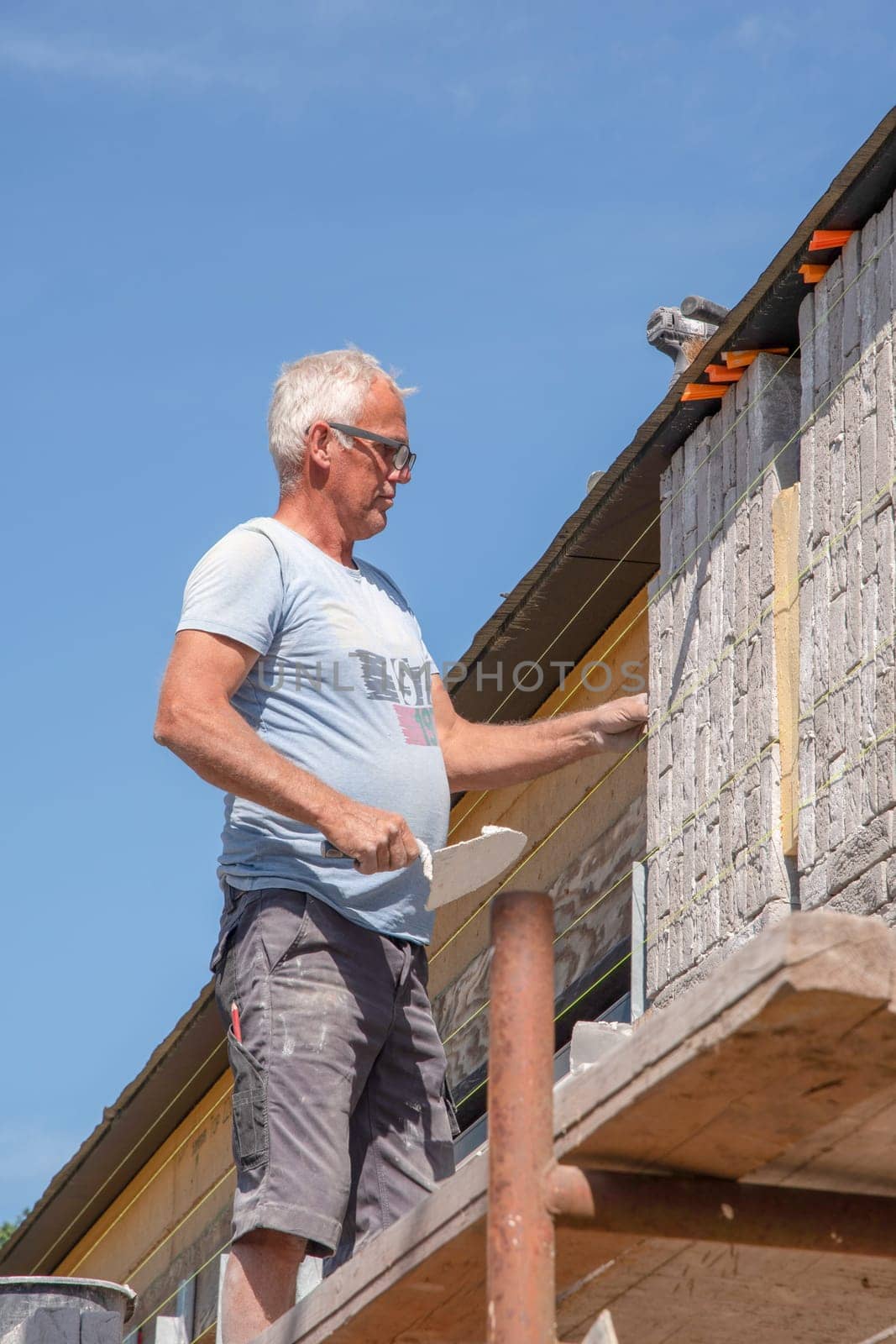 the bricklayer makes the facade of the house from gray bricks with cement and plaster at the construction site. High quality photo