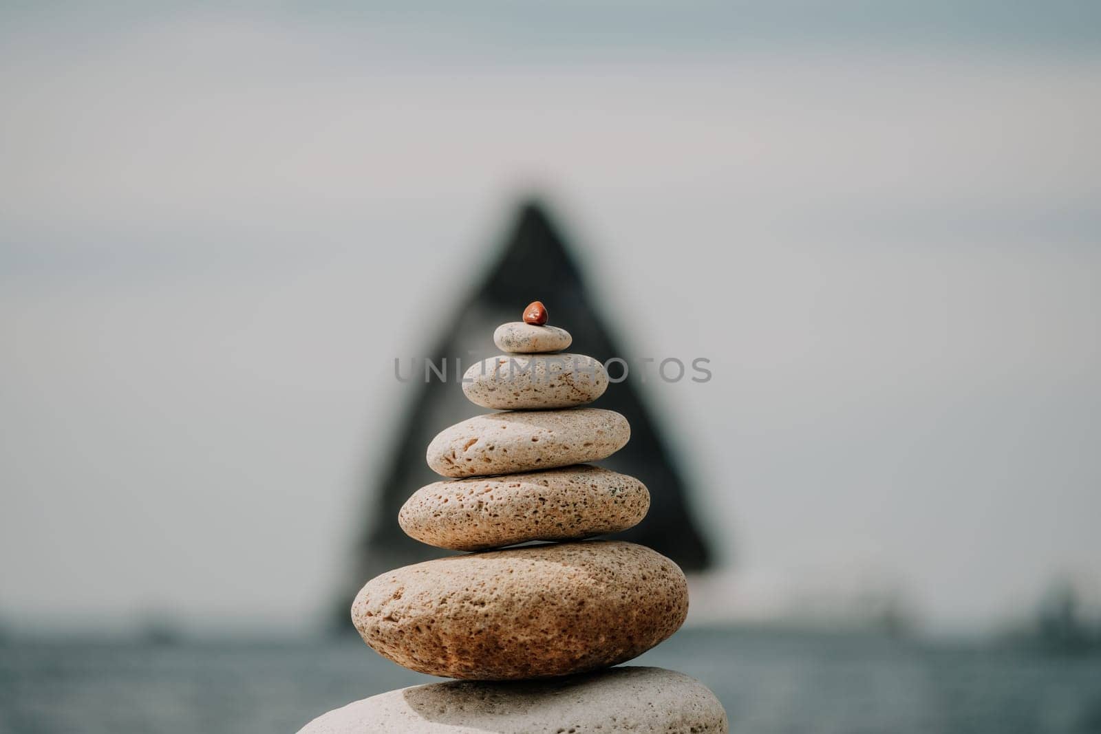 Pyramid stones on the seashore with warm sunset on the sea background. Happy holidays. Pebble beach, calm sea, travel destination. Concept of happy vacation on the sea, meditation, spa, calmness.