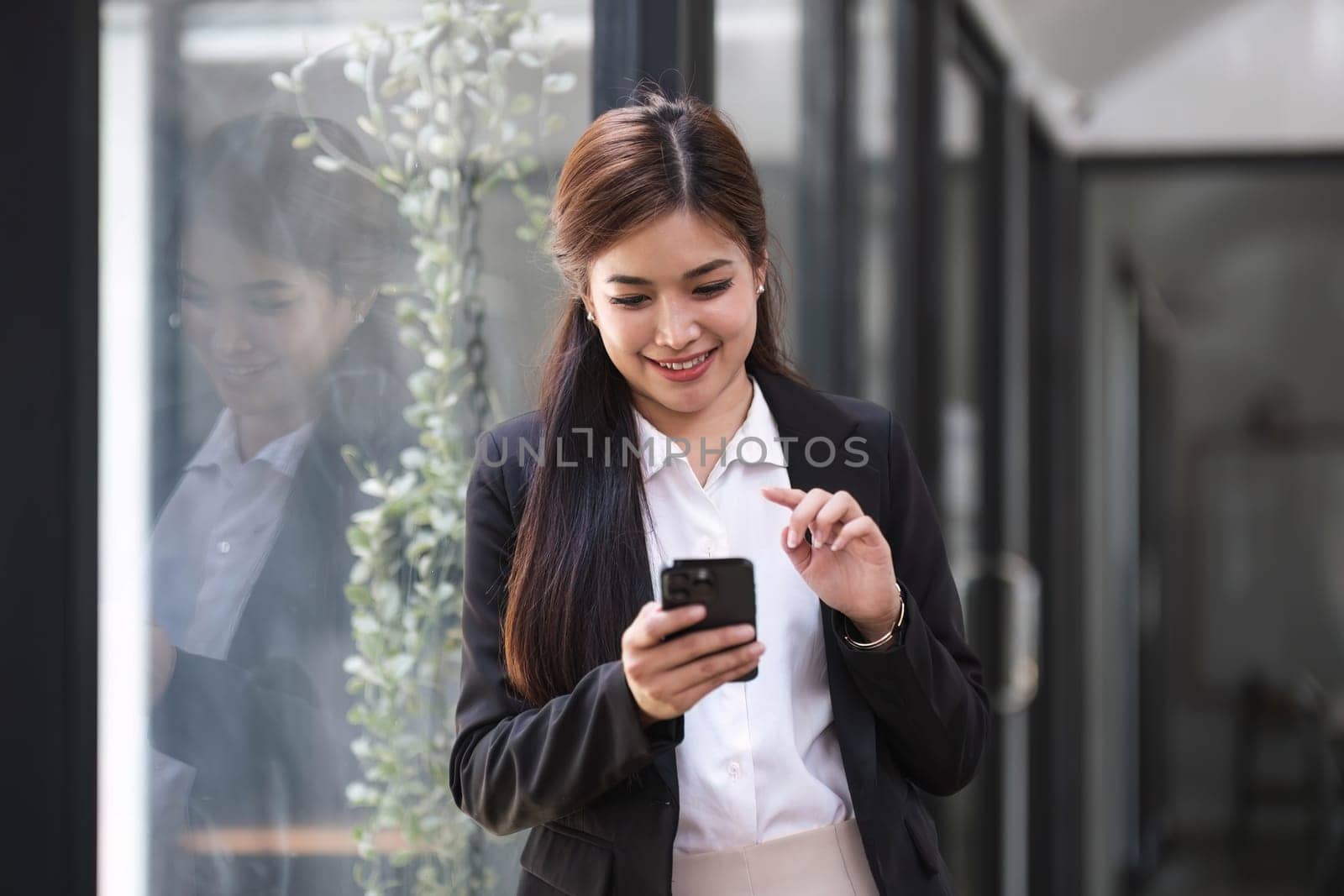 Charming Asian woman with a smile standing holding papers and mobile phone at the office...