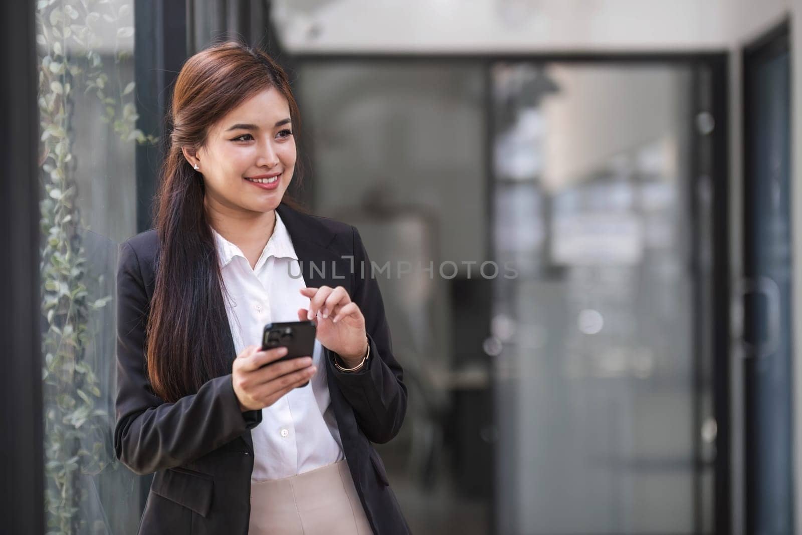 Charming Asian woman with a smile standing holding papers and mobile phone at the office...