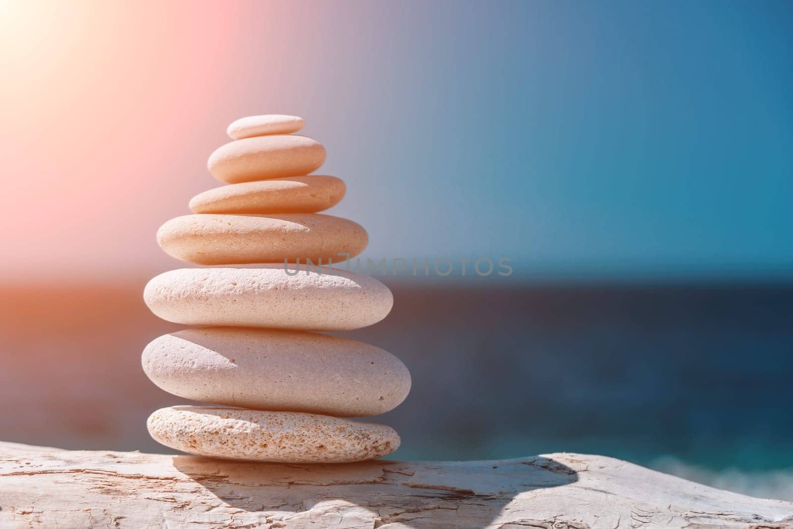 Balanced Pebbles Pyramid on the Beach on Sunny Day and Clear Sky at Sunset. Blue Sea on Background Selective focus, zen stones on sea beach, meditation, spa, harmony, calm, balance concept.