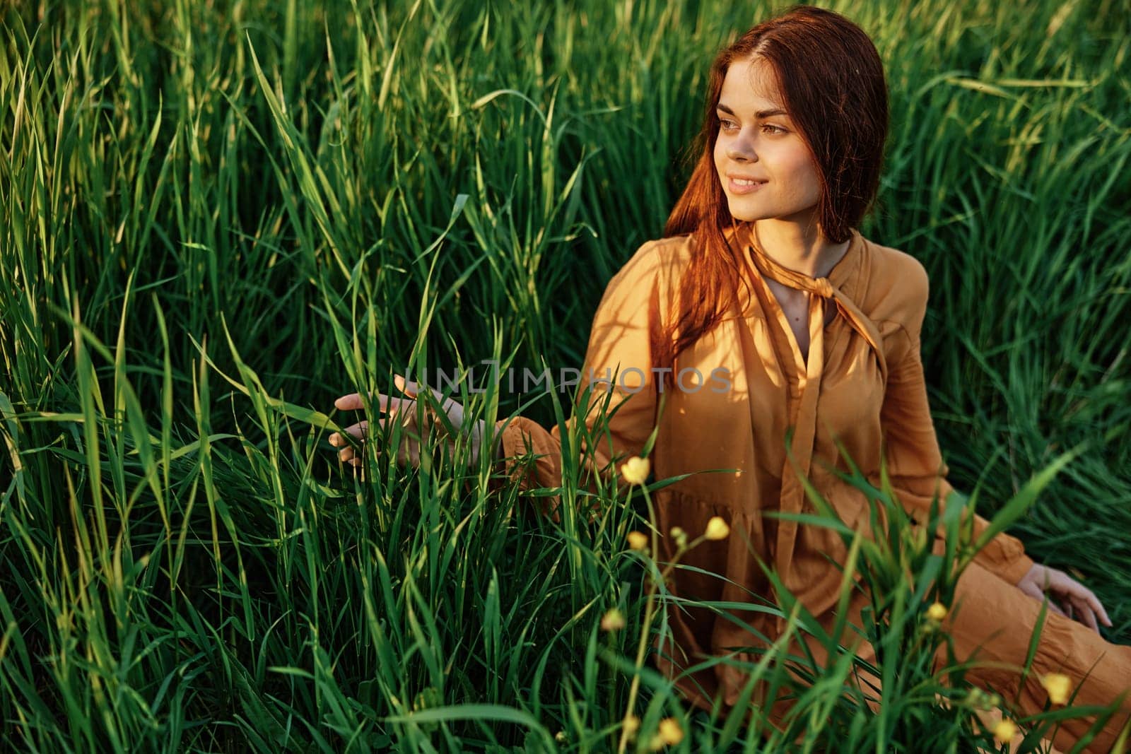 horizontal photo of a nice woman in a long orange dress resting lying in the tall grass looking to the side holding the leaves with her hand. Street photography, the theme of privacy with nature. High quality photo