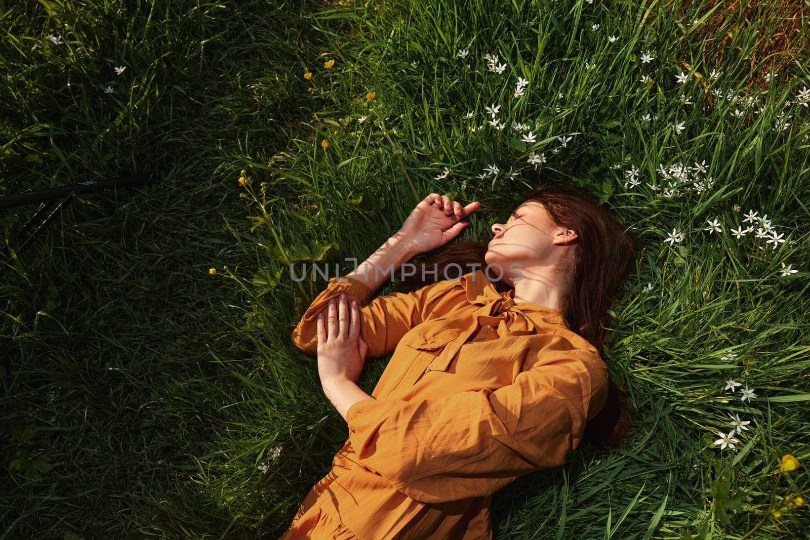 horizontal photo of a happy, relaxed woman, resting lying in the grass, in a long orange dress, with closed eyes and a pleasant smile on her face, enjoying harmony with nature and recuperating. High quality photo
