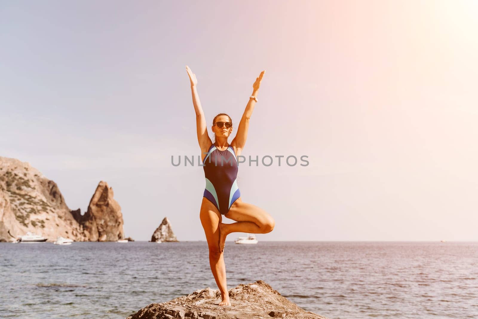 Yoga on the beach. A happy woman meditating in a yoga pose on the beach, surrounded by the ocean and rock mountains, promoting a healthy lifestyle outdoors in nature, and inspiring fitness concept