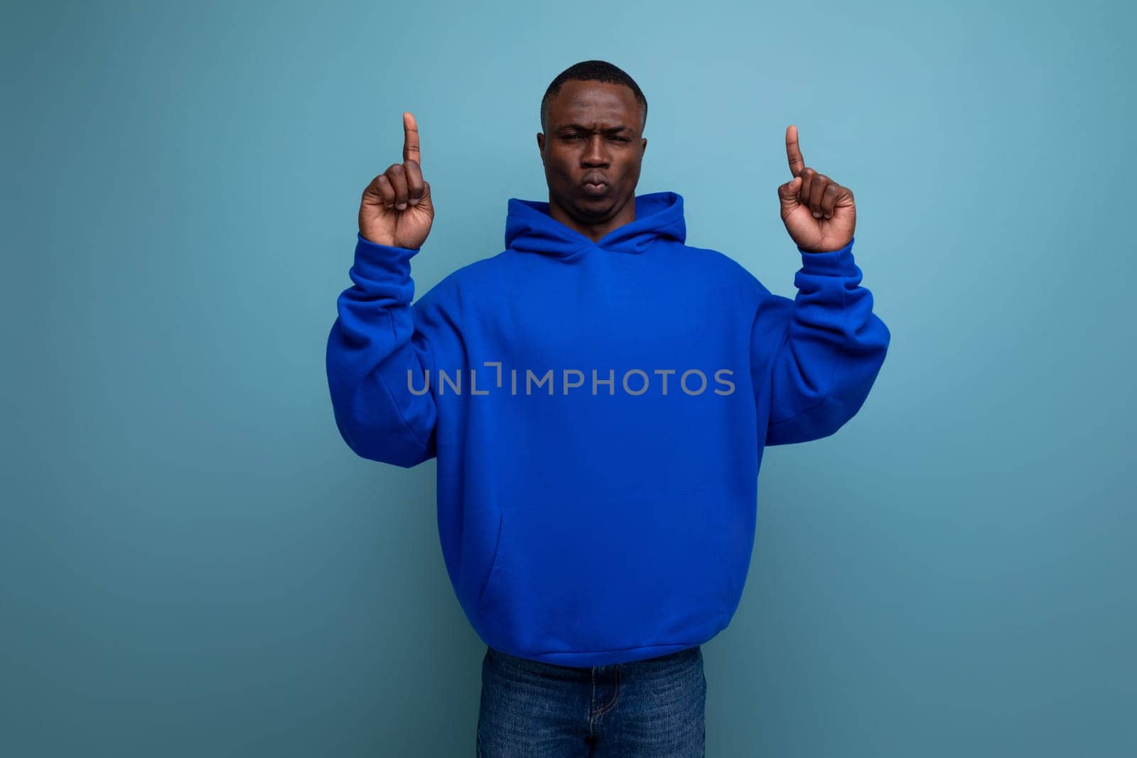 energetic positive young african man consultant in stylish hoodie shows with hand actual offer on studio background with copy space.