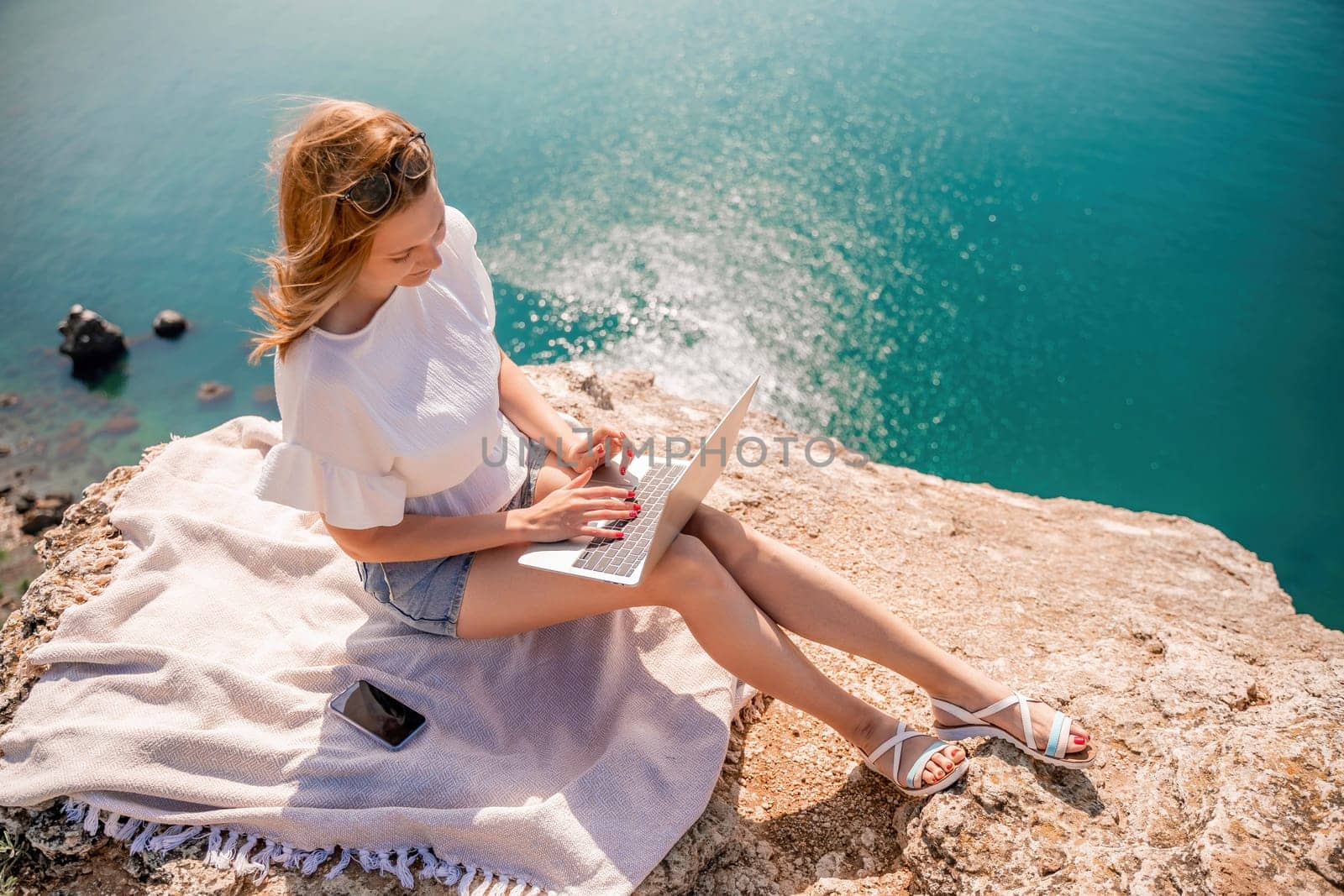 Freelance woman working on a laptop by the sea, typing away on the keyboard while enjoying the beautiful view, highlighting the idea of remote work