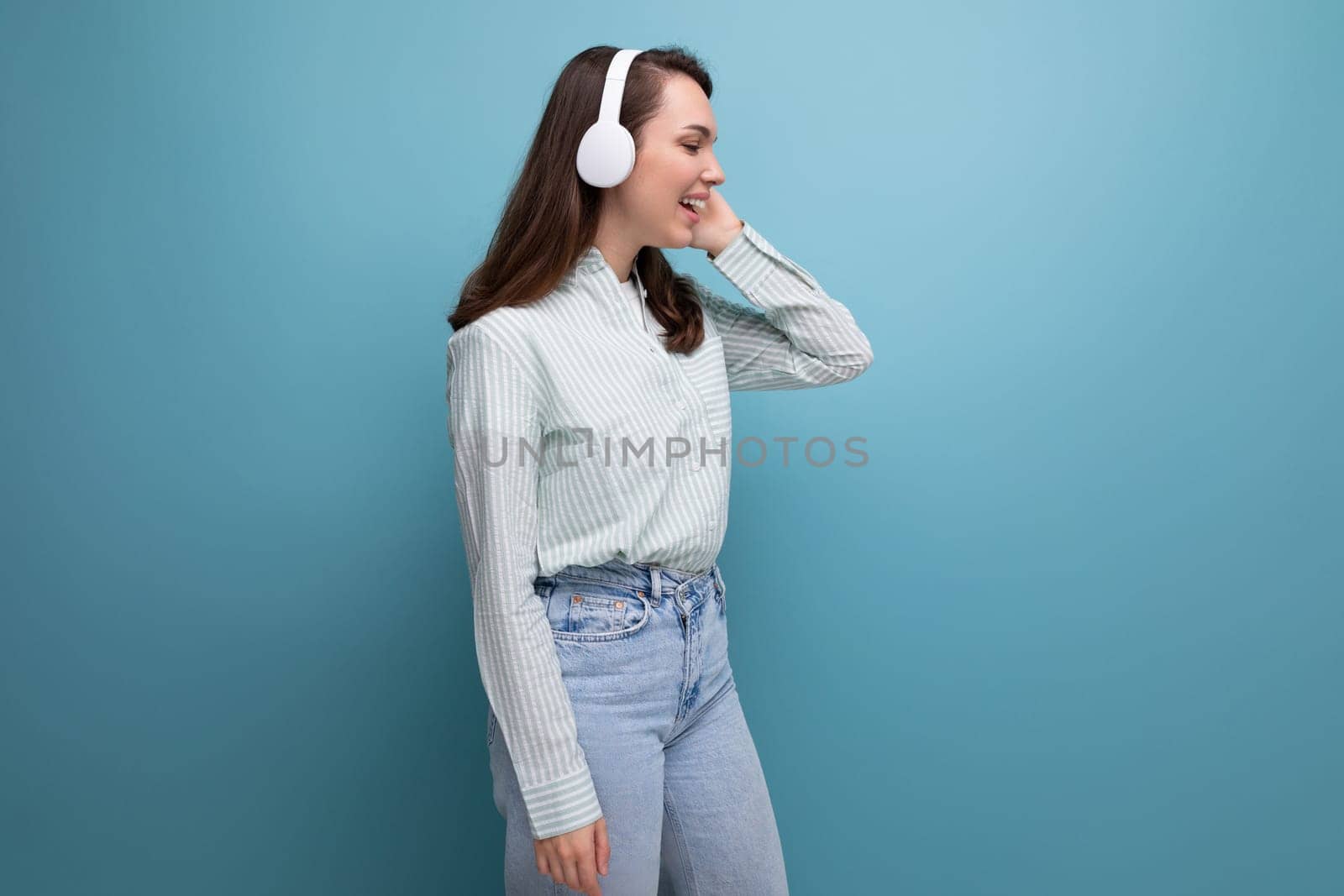 20s brunette lady in shirt and jeans listening to playlist in wireless headphones.