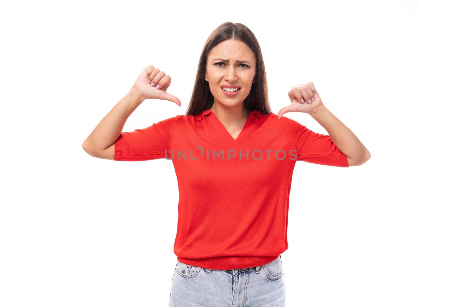 young brunette lady in a red t-shirt looks confusedly at the camera on a white background with copy space by TRMK