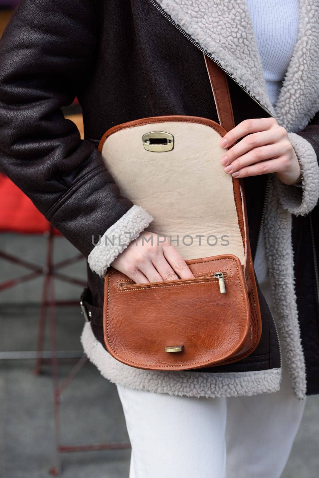 woman in white pants and a beige sweater poses outside with a small leather handbag by Ashtray25