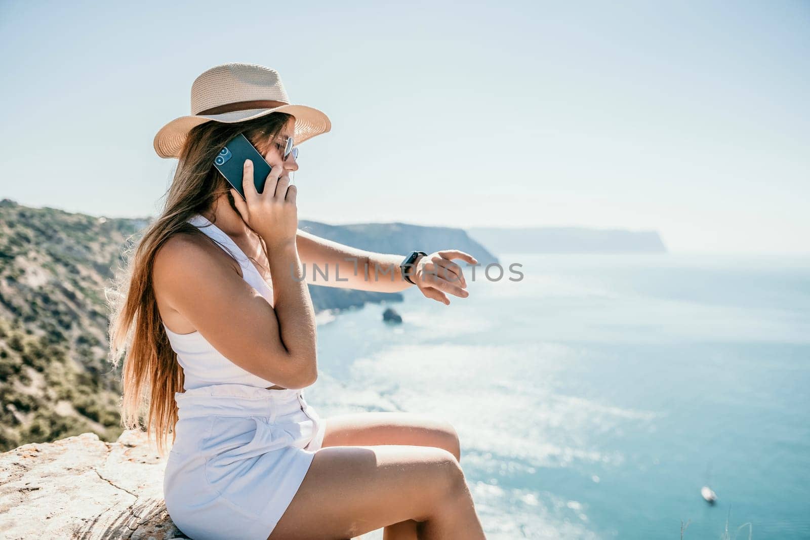 Successful business woman in yellow hat working on laptop by the sea. Pretty lady typing on computer at summer day outdoors. Freelance, travel and holidays concept.