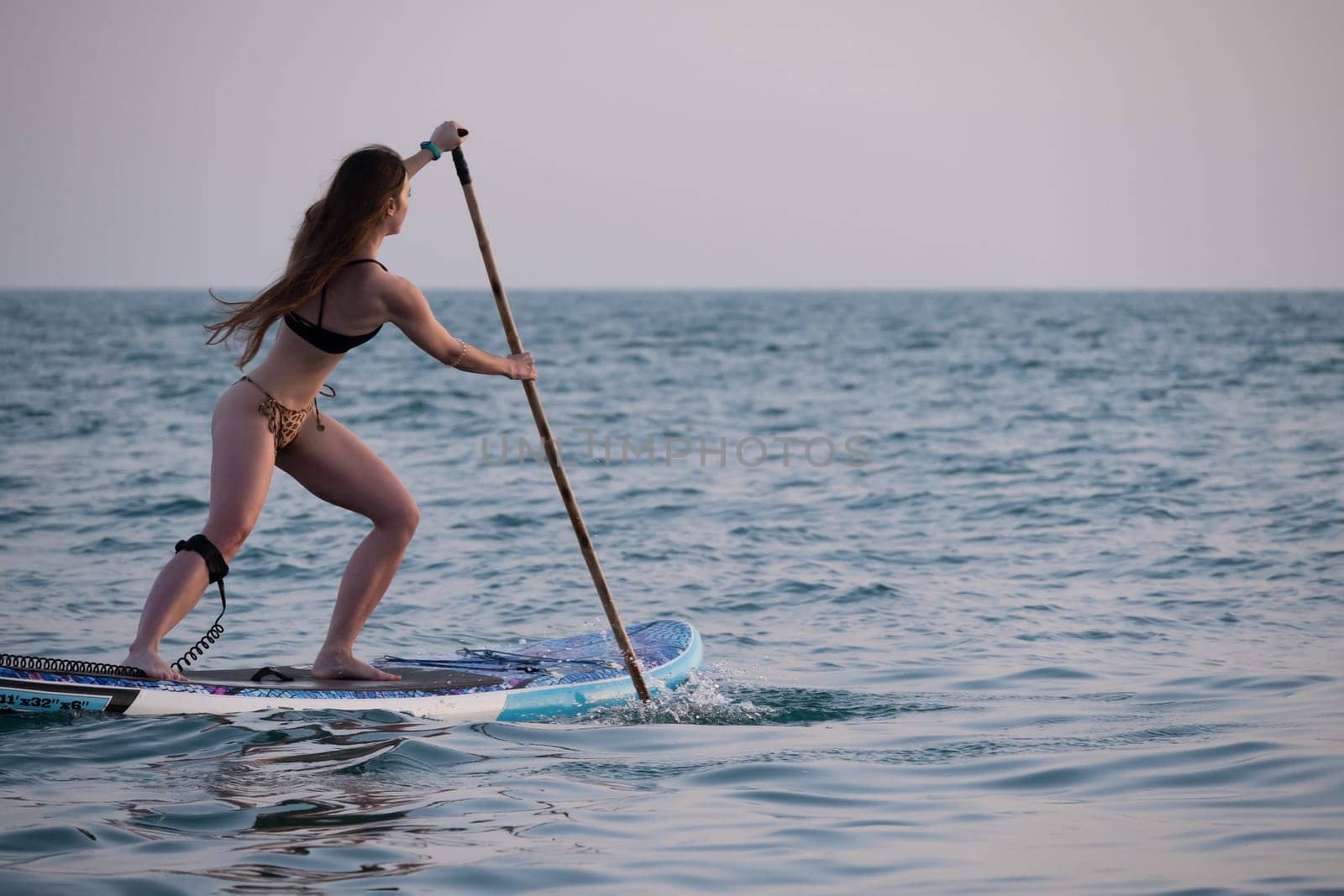 sexy girl on a sup board in the sea with paddle professionally swims beautifully and gracefully