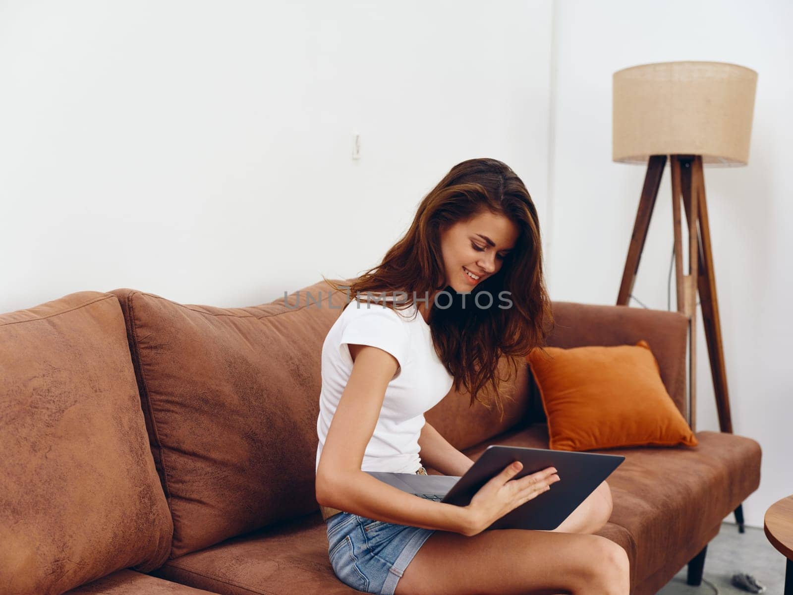 Woman freelancer sitting on the couch with a laptop beautiful smile , modern stylish interior Scandinavian lifestyle, copy space. by SHOTPRIME