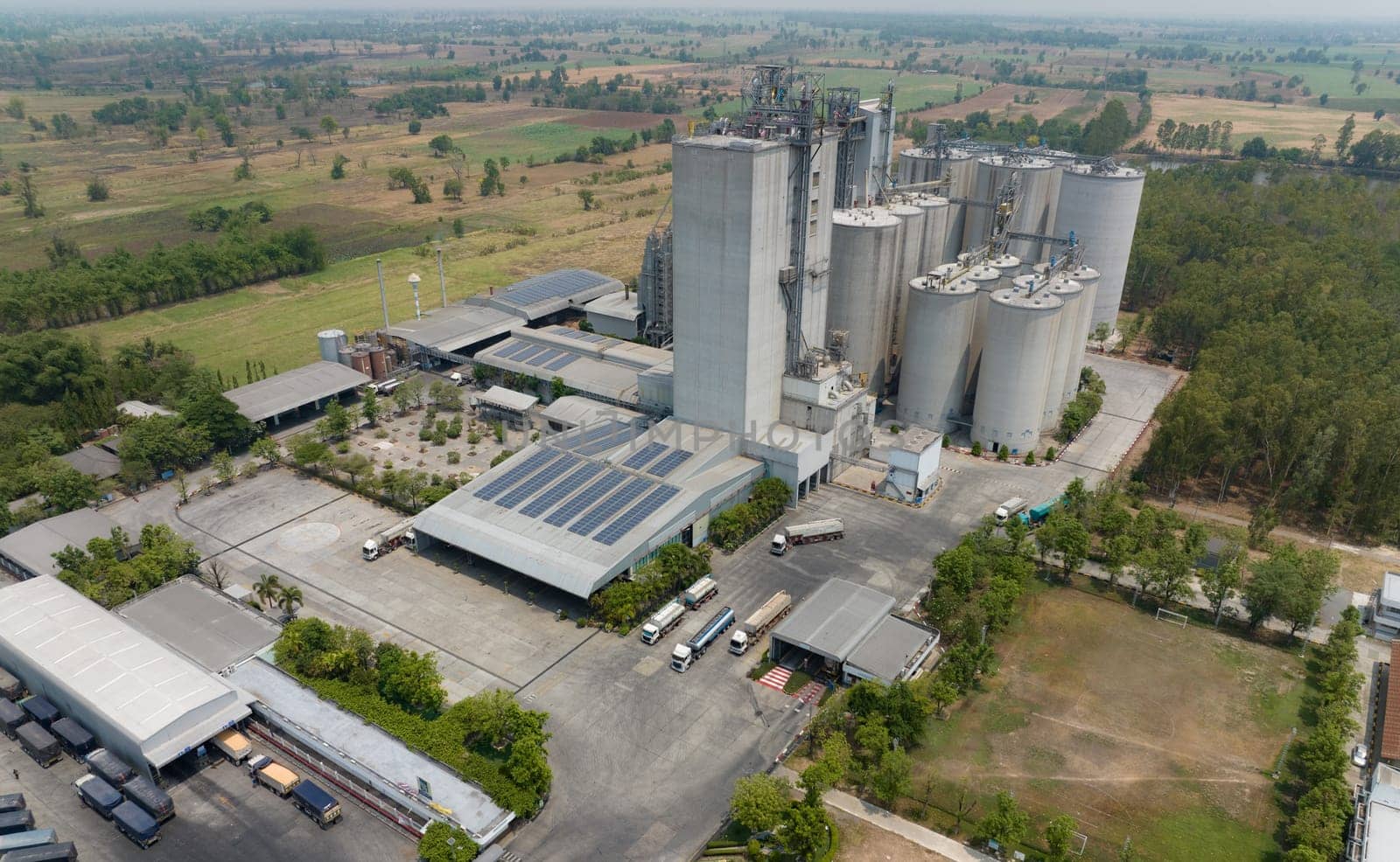 Aerial view of animal feed factory. Agricultural silos, grain storage silos, and solar panel on roofs of industrial plants. Industrial landscape. Agriculture industry. Factory with sustainable energy. by Fahroni