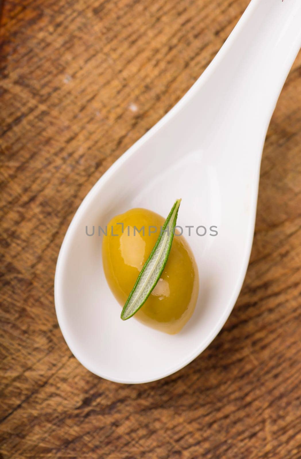 Close up green olives in bank, bottle of olive oil, rosemary on a wooden background