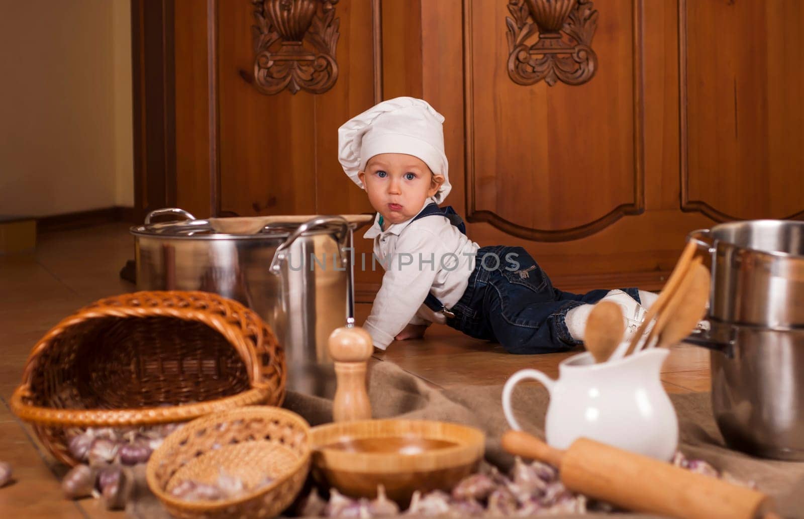 Little boy in chef's hat with ladle, pan and vegetables