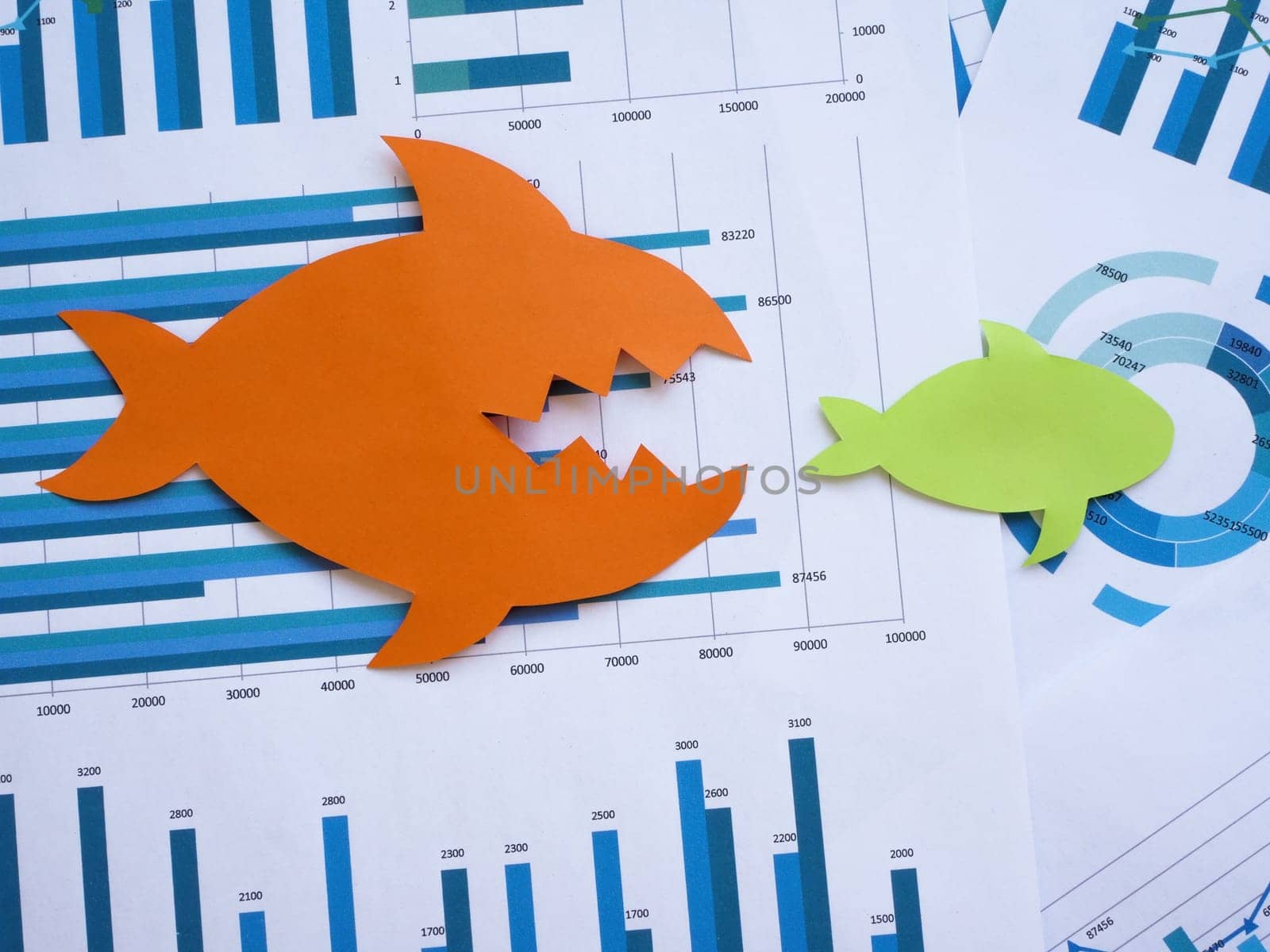 Mergers and acquisitions concept. Two paper fish on financial charts.