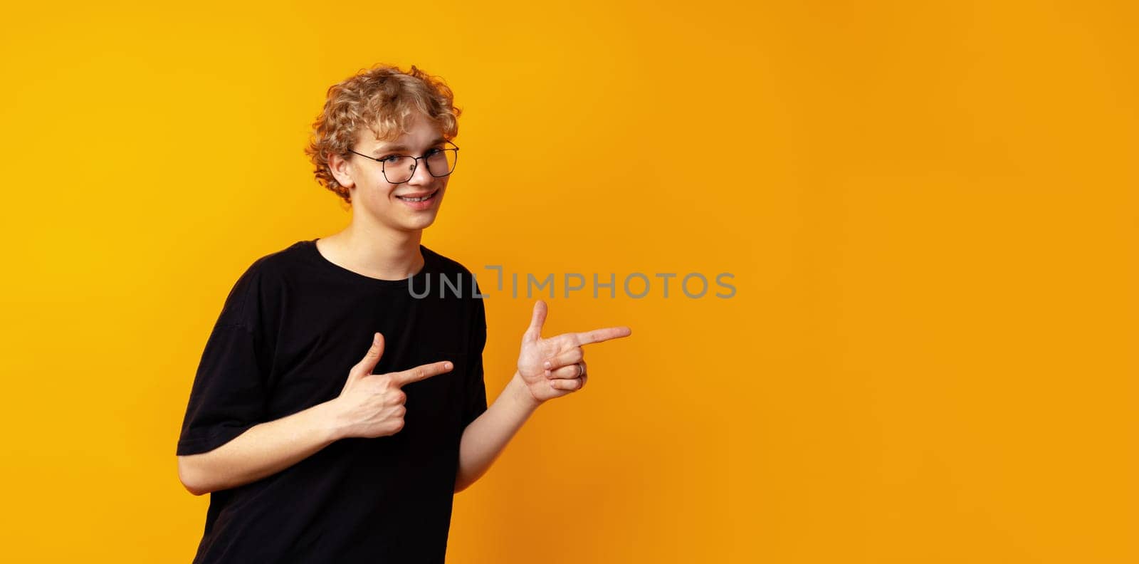 Handsome young man pointing finger to copy space on yellow banner background by Fabrikasimf