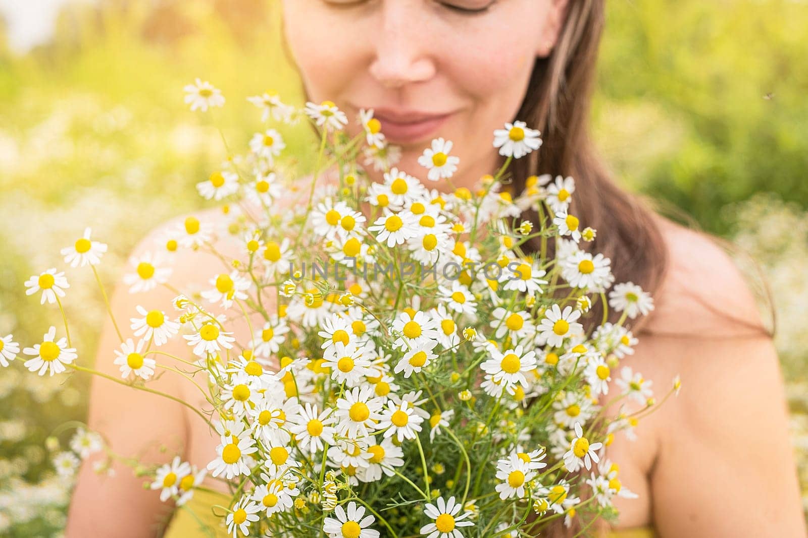 Woman holds daisies in her hands in the field in summer day