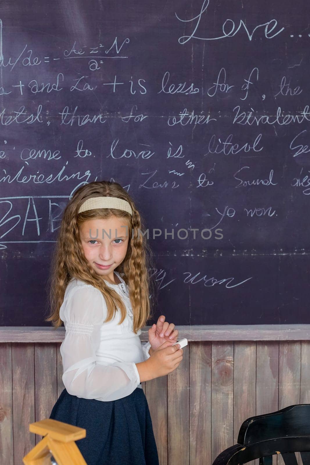 little girl in a white blouse with pigtails writes with chalk on black chalkboard back to school