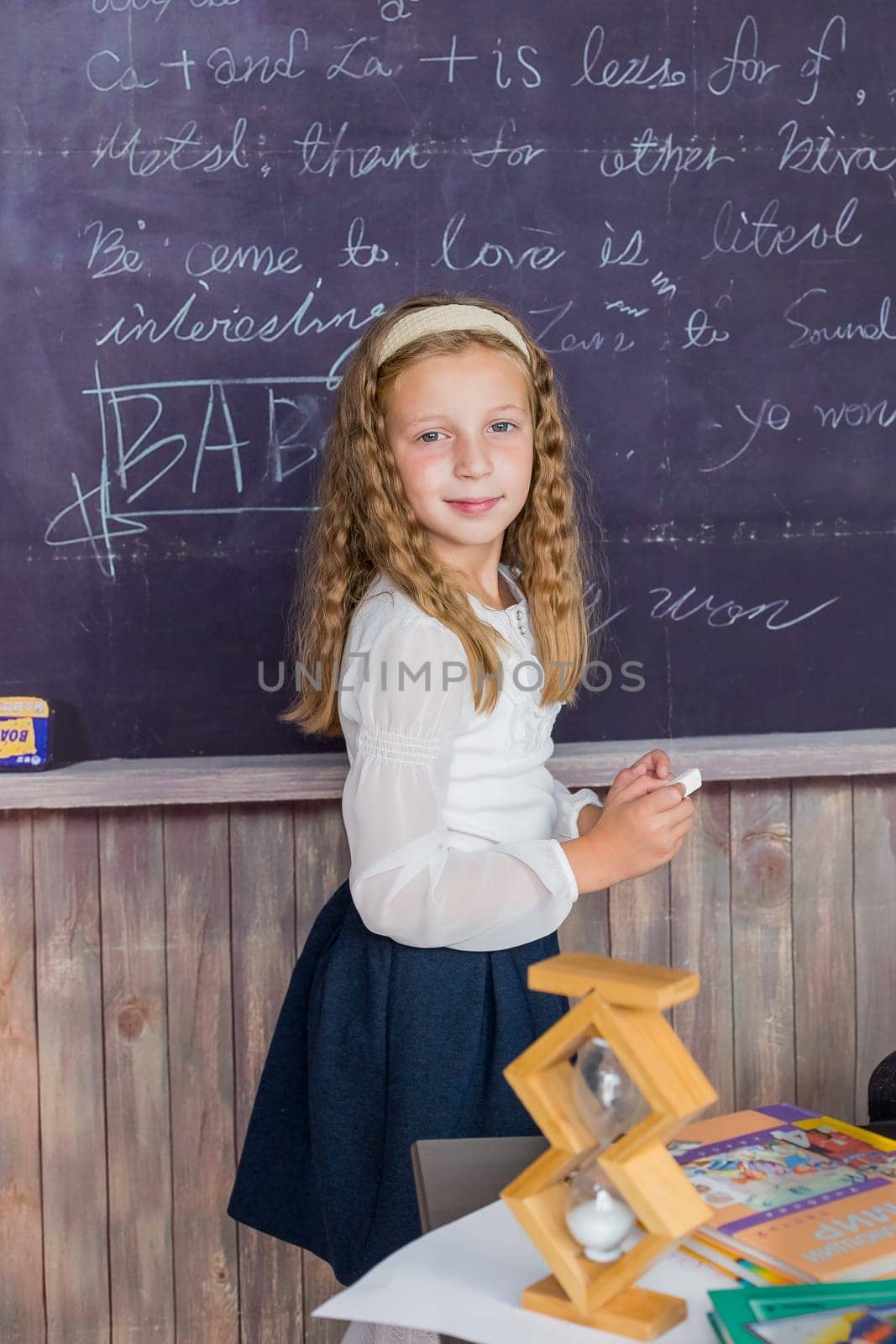 little girl in a white blouse with pigtails writes with chalk on black chalkboard back to school