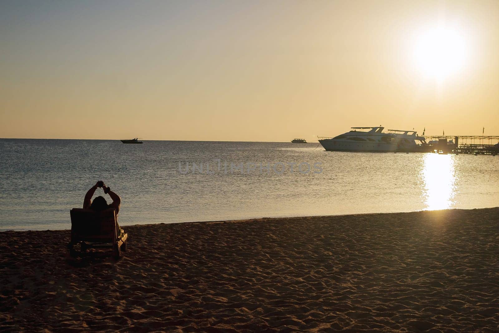 Young woman relaxing in a deck chair on the beach in the morning, meeting the dawn.