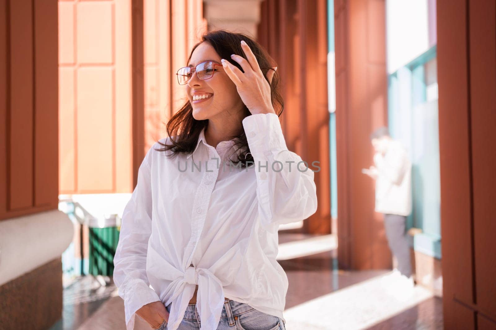 Successful smiling business woman wearing eyeglasses correct hairstyle by hand. Modern businesswoman smile standing outdoor dressed white shirt looking away. Business woman happy positive emotions