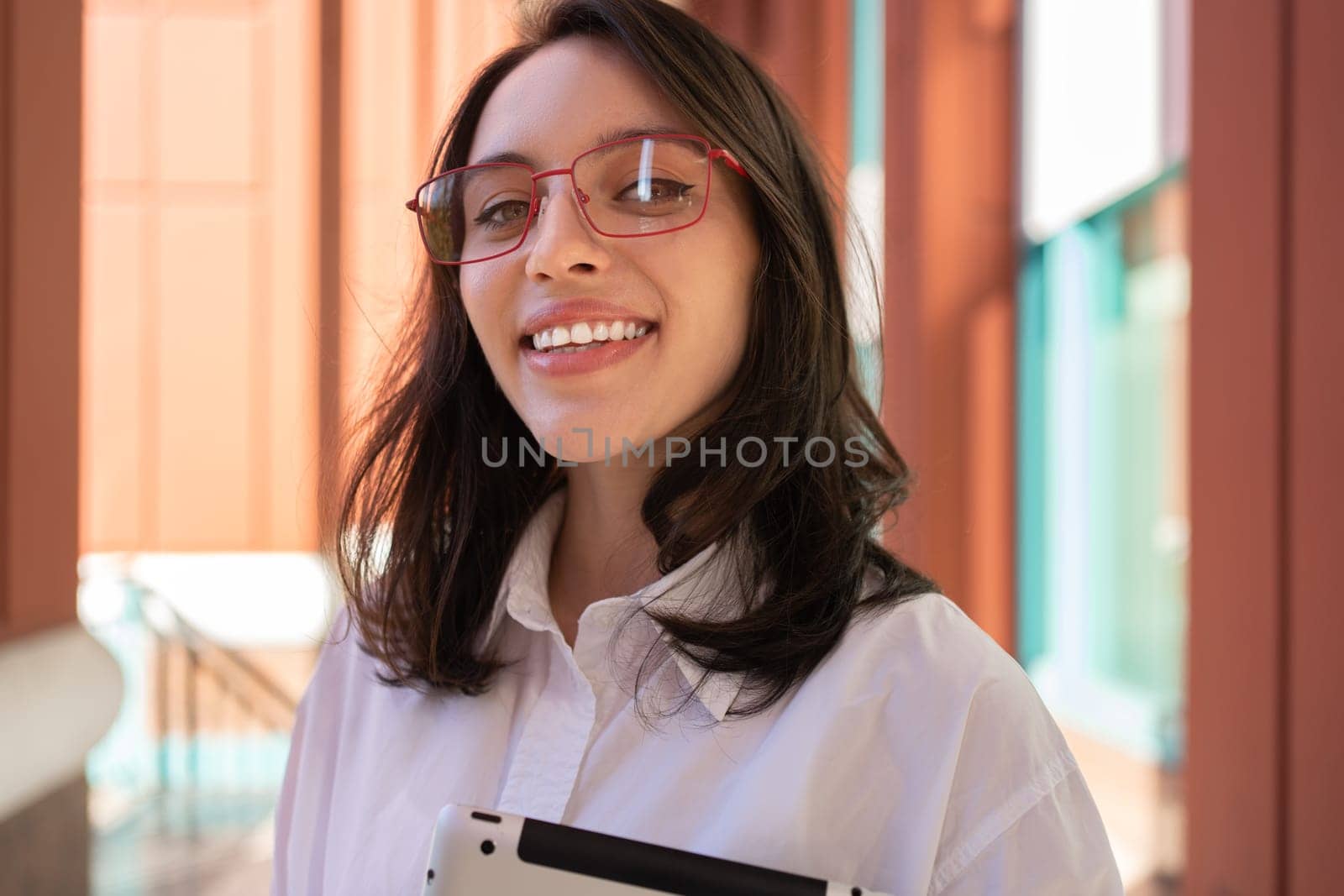 Businesswoman in glasses looking at camera, smiling and holding digital tablet, standing outdoor. Female freelancer holding tablet while walk outside close up portrait