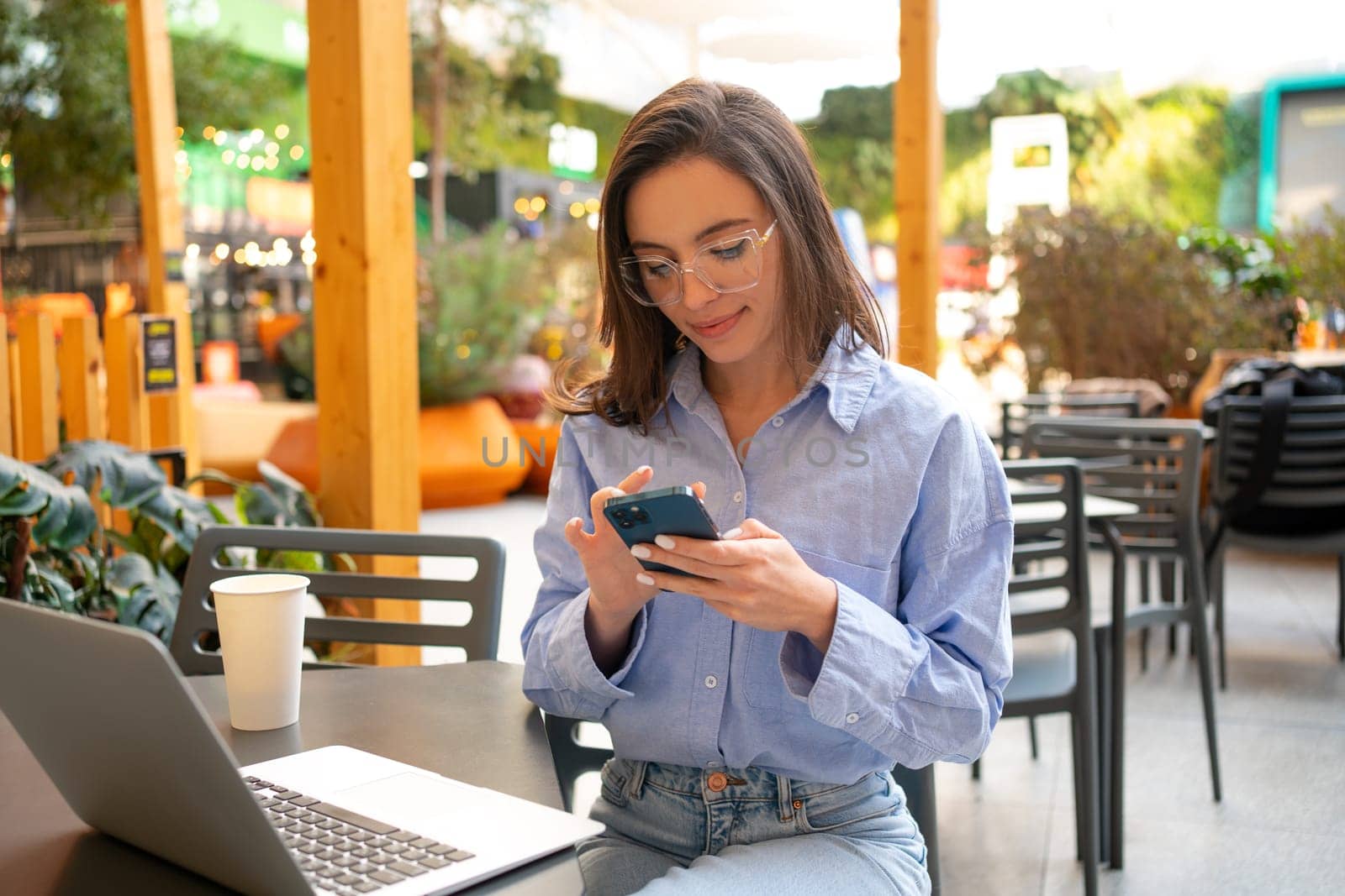 Freelance worker doing remote work planning on mobile 5g smartphone internet schedule. Woman entrepreneur with mobile phone in outdoor cafe, restaurant on social media app online.