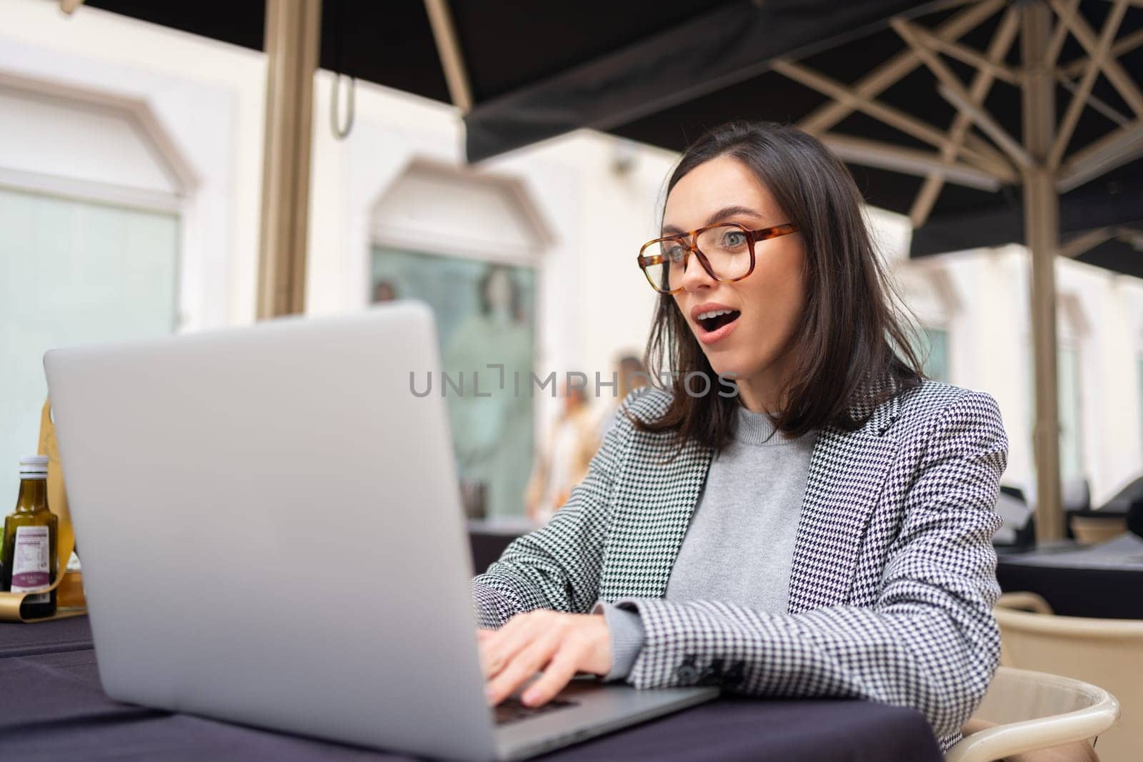 Woman working on remote from outdoor cafe, sitting with laptop on restaurant terrace on city street, studying. Excited positive female freelancer using laptop