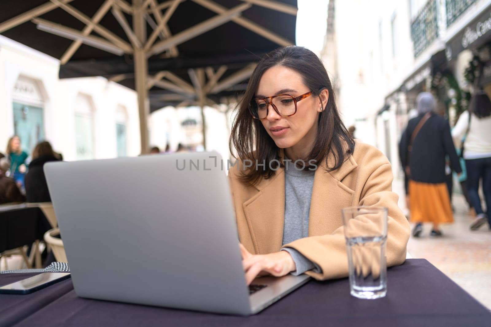 Woman working on remote from outdoor cafe, sitting with laptop and smiling, studying.