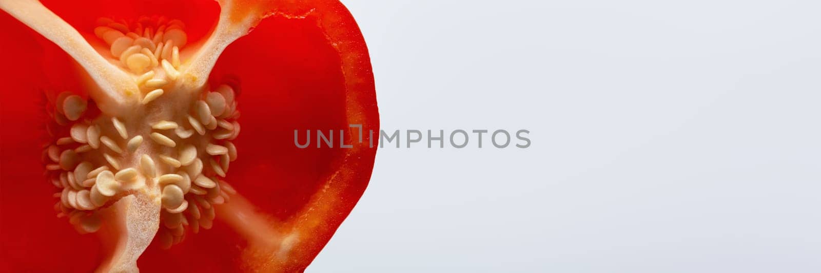 Paprika seeds close-up. A large fresh red paprika is cut in half and its seeds are visible with copy space. by SERSOL