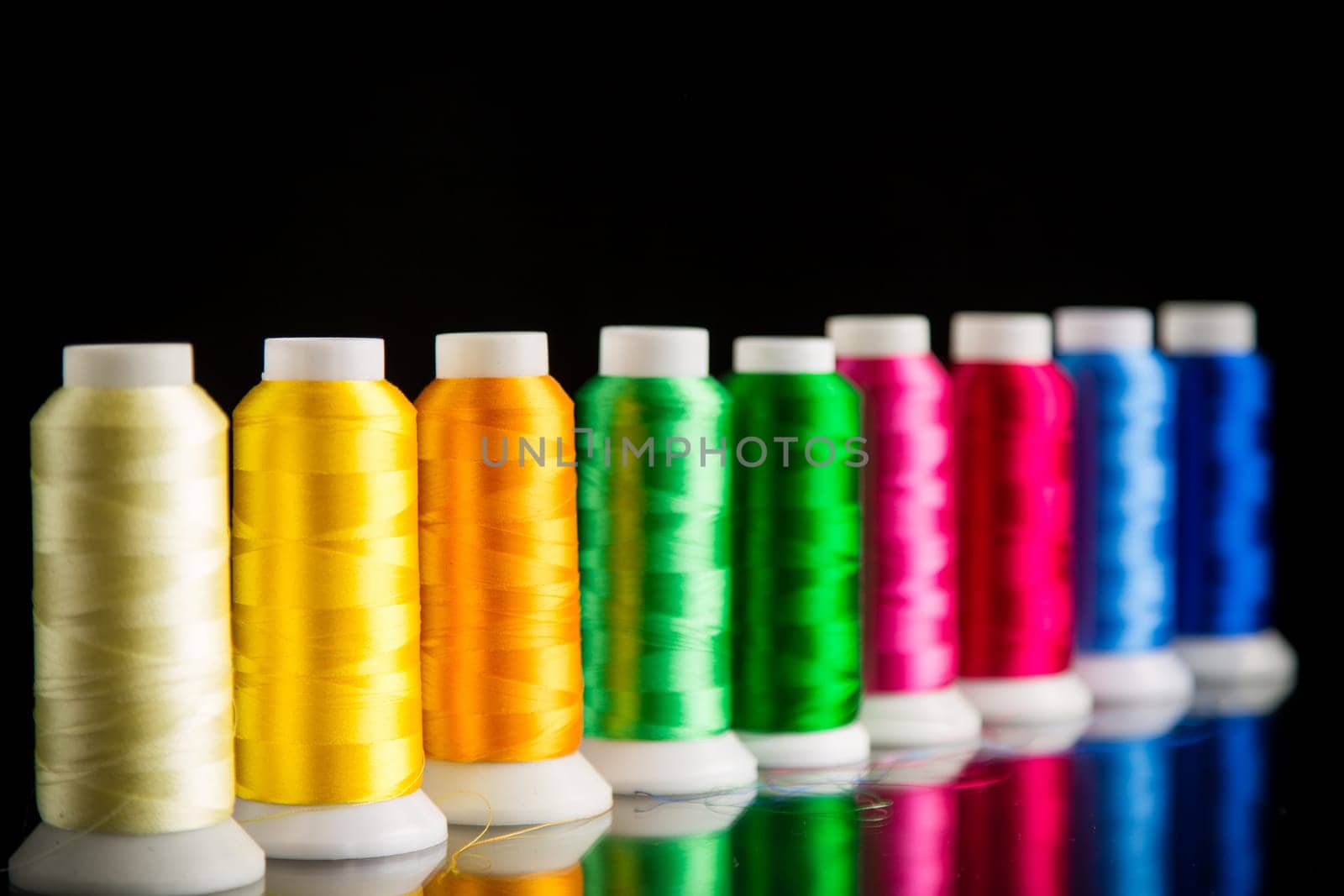 set of different color sewing threads, isolated on black background.