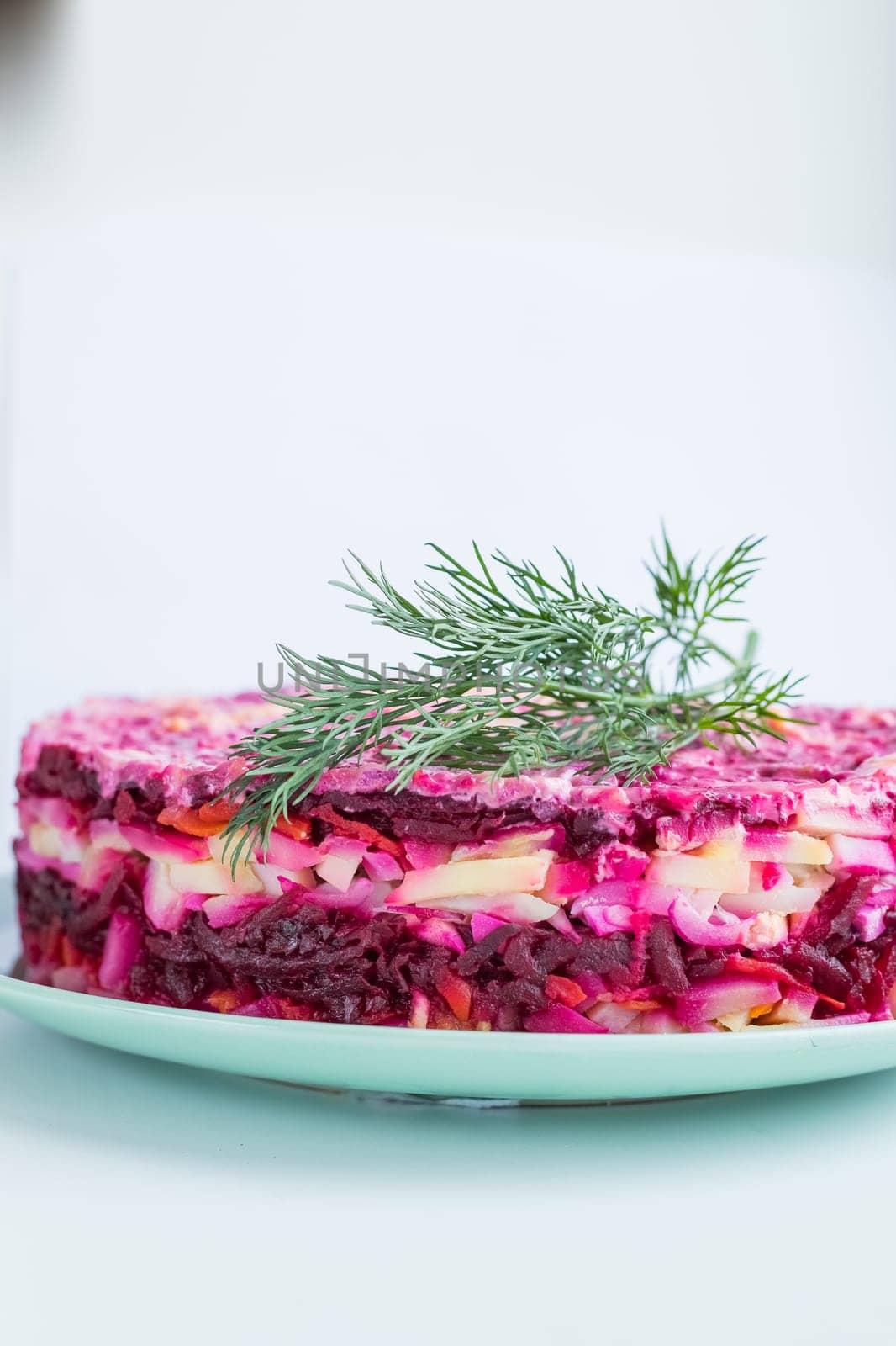 Russian salad - herring under a fur coat, herring salad with potatoes, eggs, beets, carrots, and mayonnaise on a white square plate