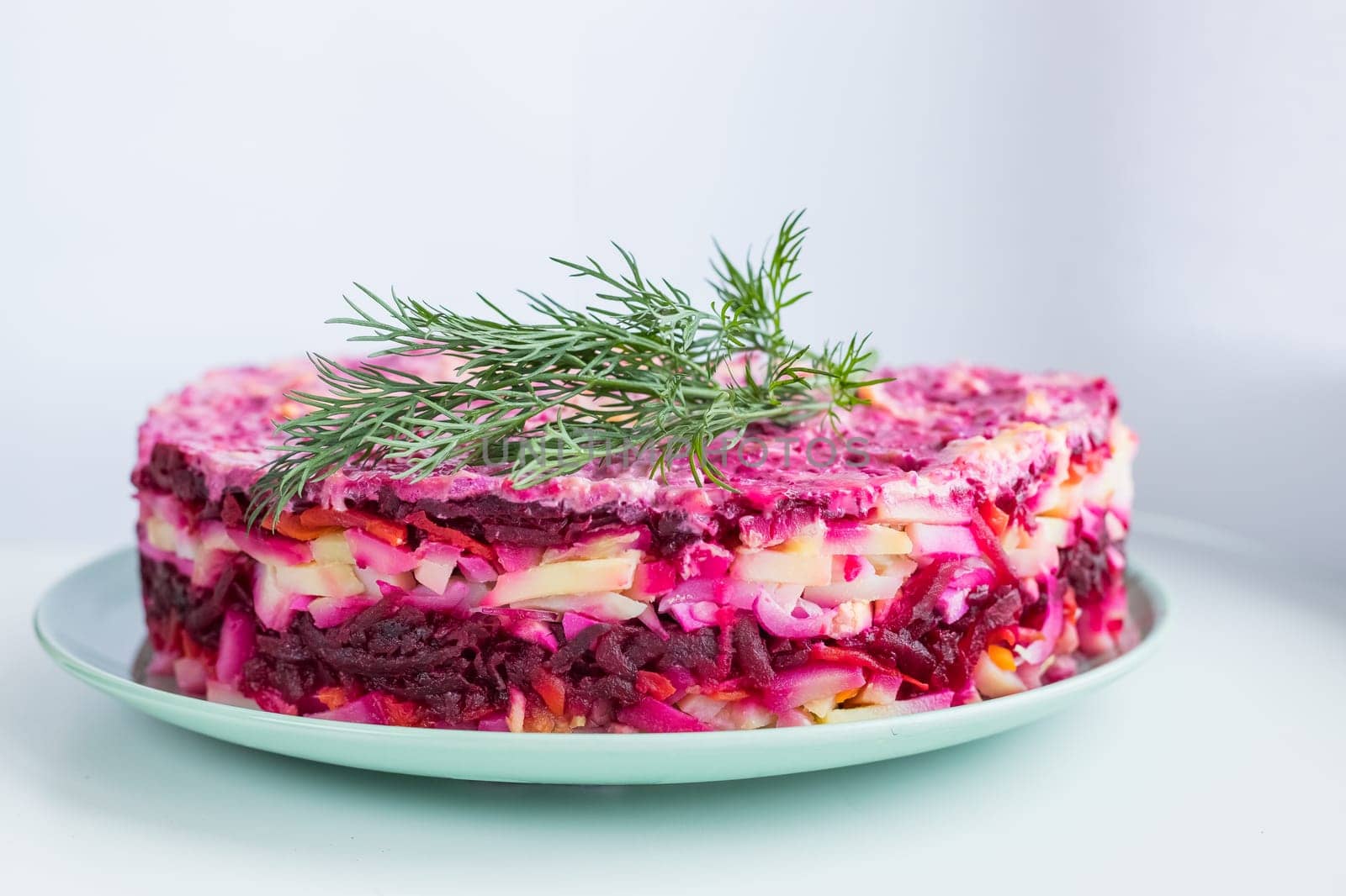Russian salad - herring under a fur coat, herring salad with potatoes, eggs, beets, carrots, and mayonnaise on a white square plate