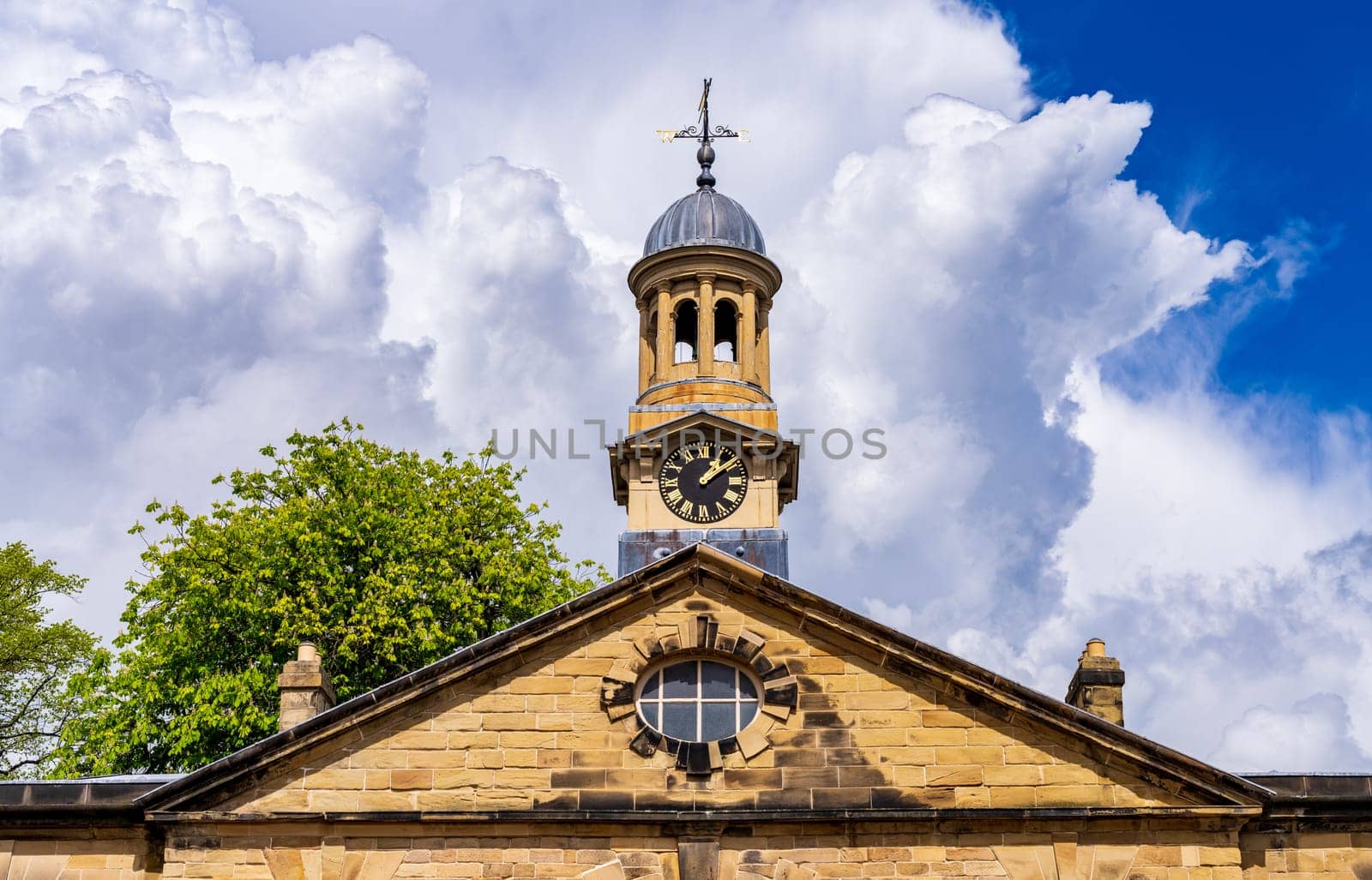 Sun shines on stone historic clock tower with dramatic sky behind in UK