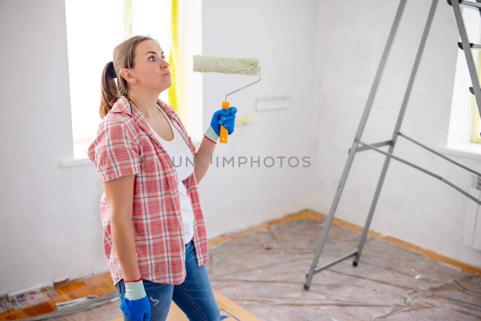 People renovation and home improvement. Positive satisfied woman holding dirty roller after painting walls in room