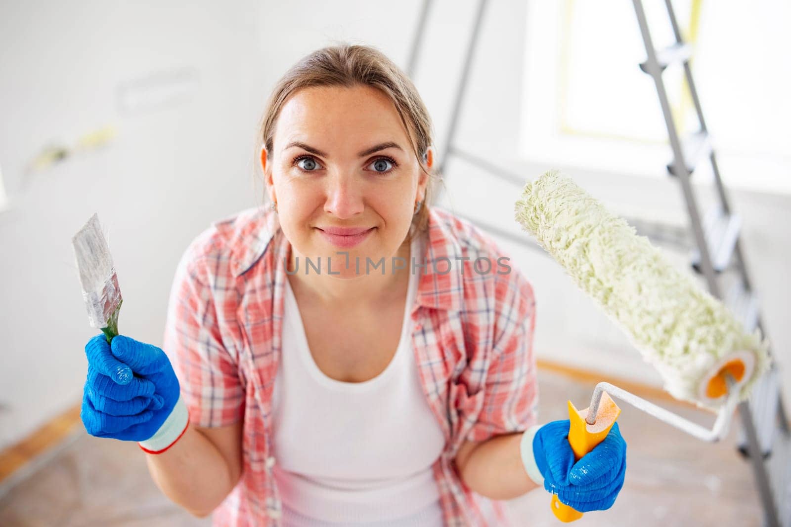 People renovation and home improvement. Positive satisfied woman holding dirty roller and brush after painting walls in room