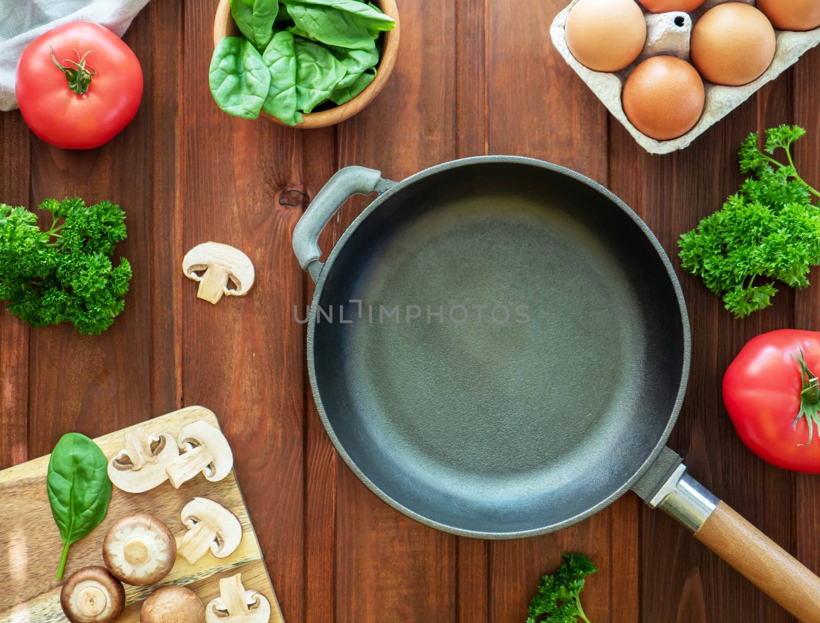 Idea for breakfast. Empty cast-iron frying pan and ingredients for omlette or scrambled eggs. Eggs, mushrooms, tomato, spinach and parsley on wooden table. Healthy homemade dish for low carb. Top view