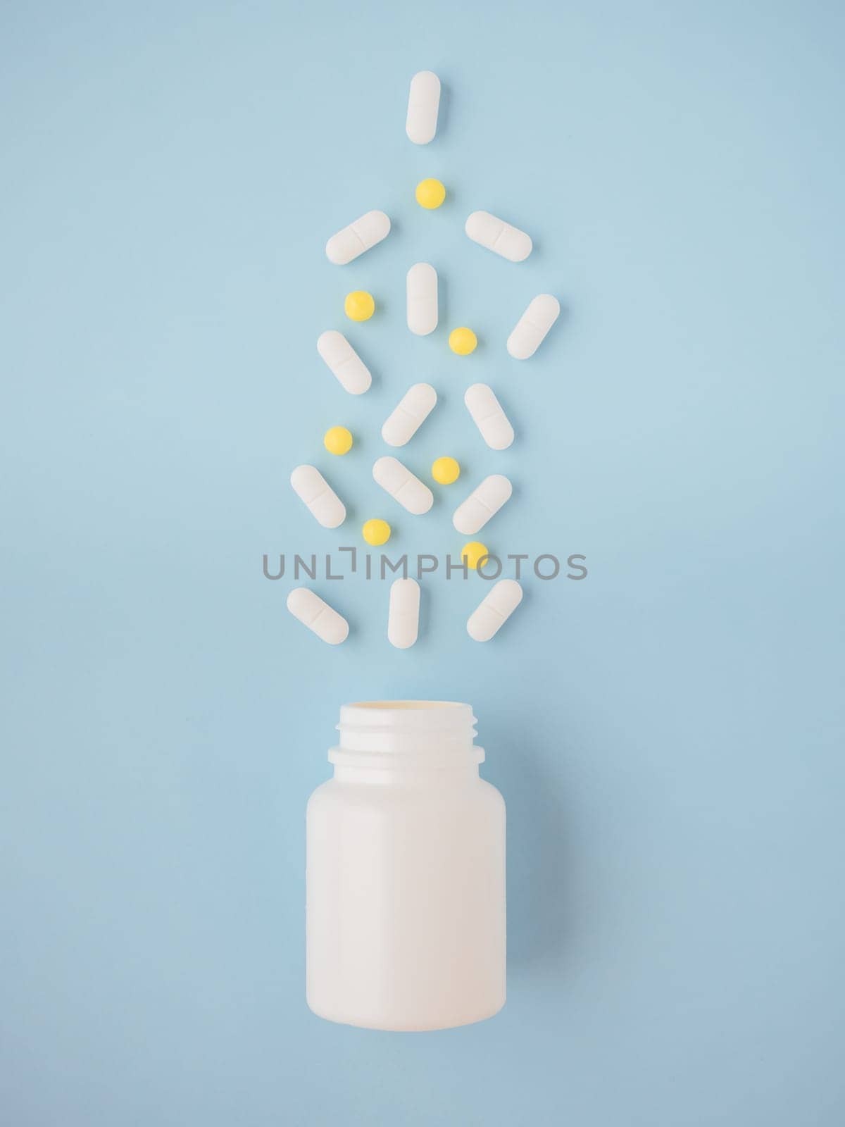Modern medicine for preventing and treat diseases. White medicine bottle, yellow and white pills on blue paper background. Vertical top view, copy space. Concept of healthcare and treatment of viruses