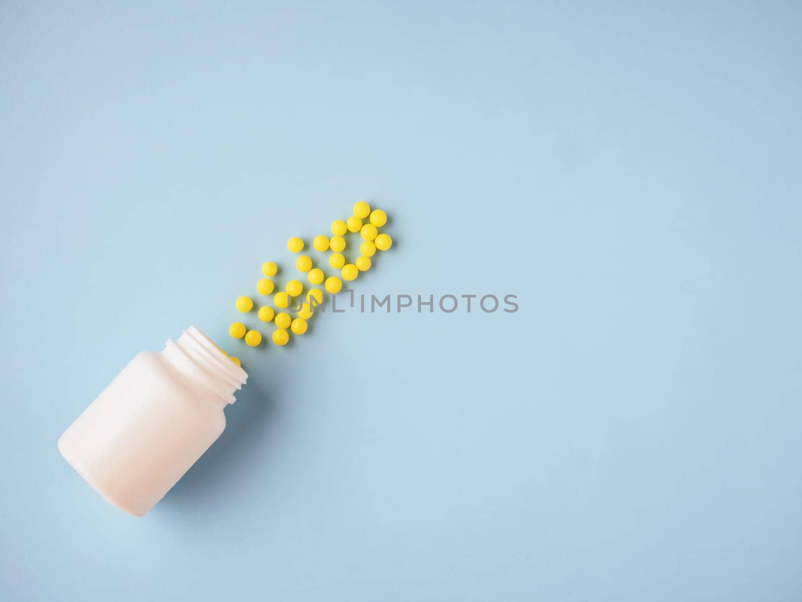 Pharmaceutical and health care concept. Minimalism style template for medical blog. White medicine bottle and small round yellow pills spilled out blue paper background. Medicine pills. Flat lay