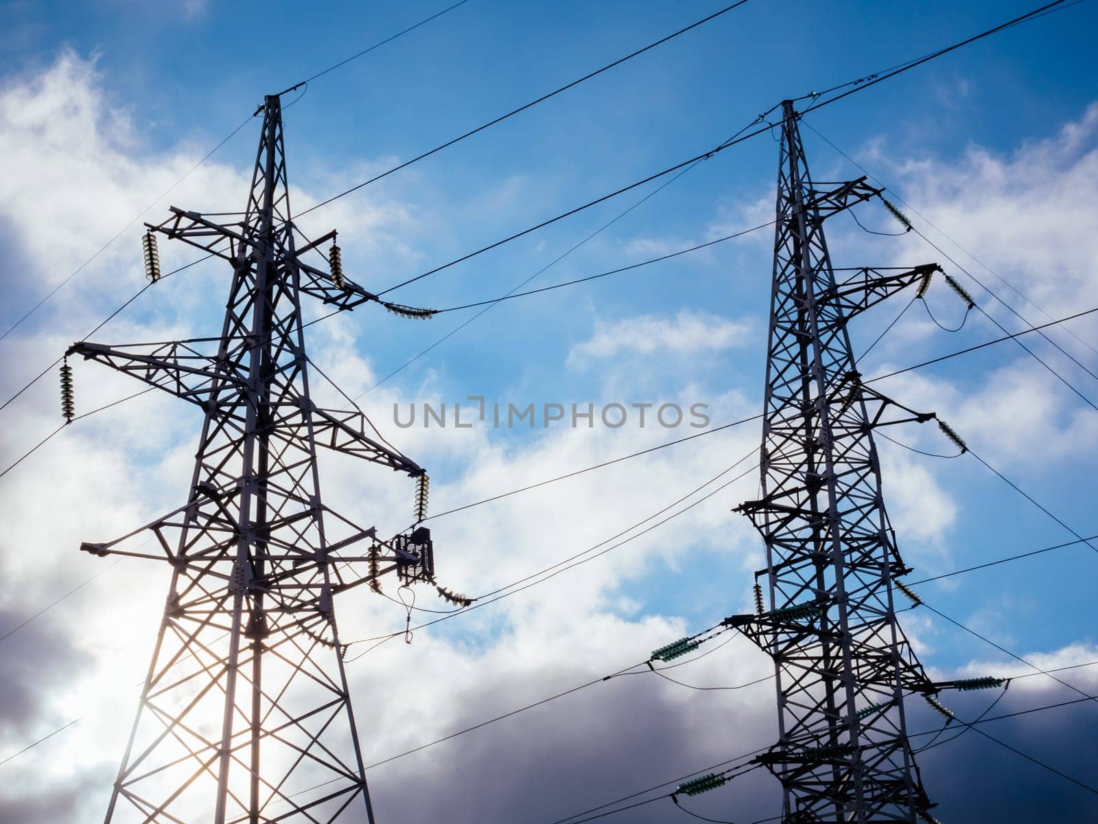 High tech power lines. High voltage electricity pillars on the blue sky background with clouds. Metal bearing high voltage power line.