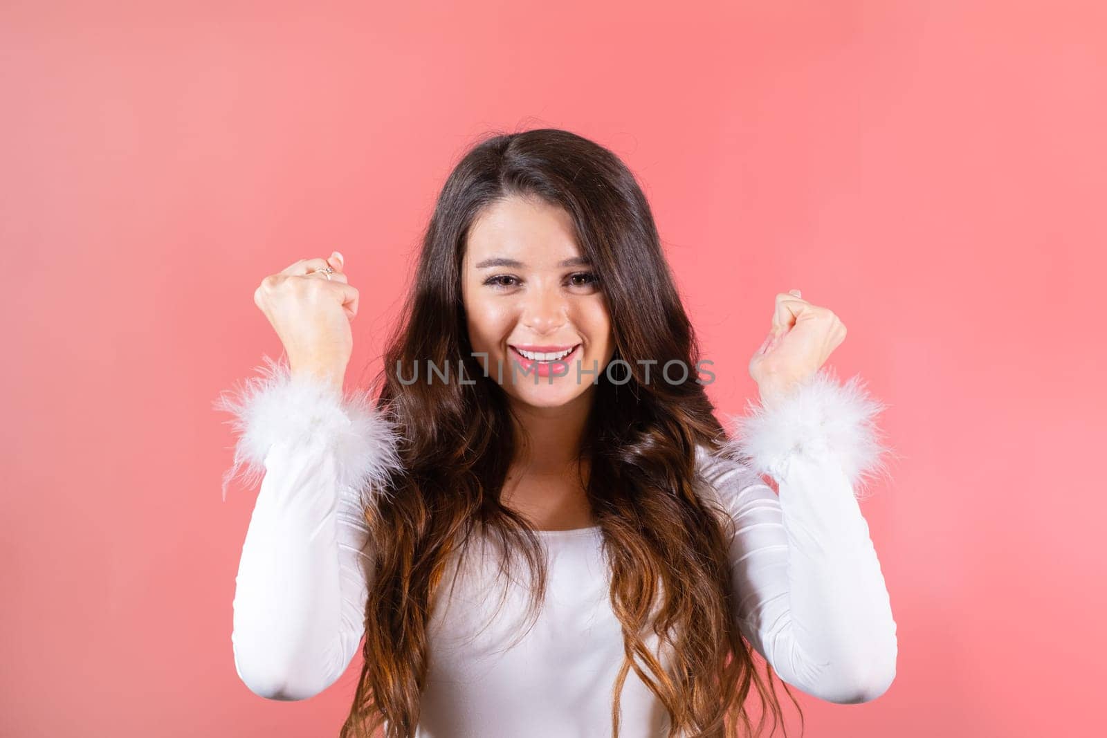 Brown-haired woman raising arms dances at loud party at pink studio wall. Smiling amused lady shows funny dance moves at friends party