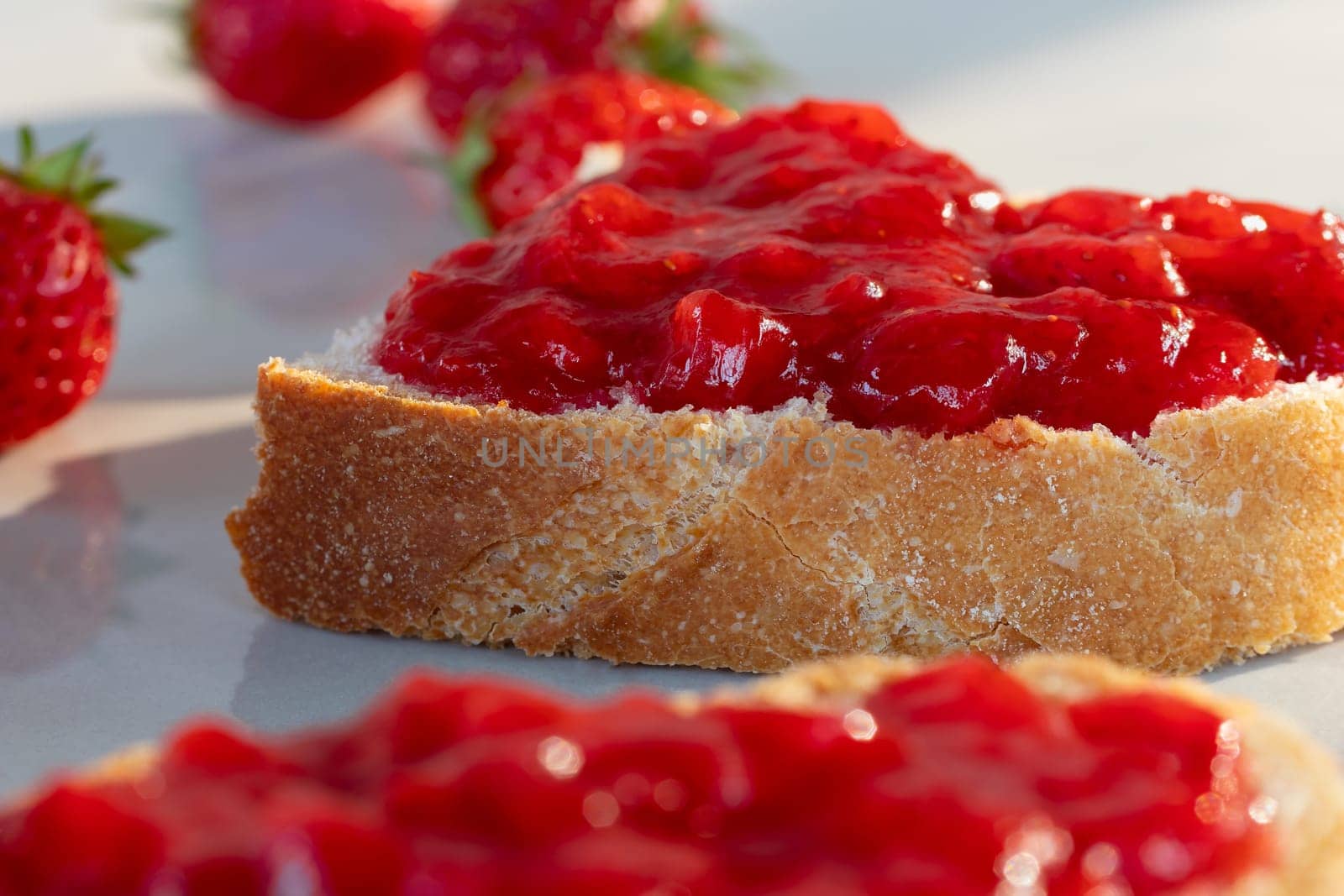 Wheat bread toasts with spread strawberry jam on the table, closeup.