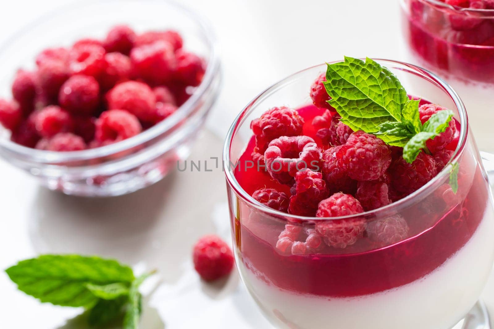 Panna cotta with raspberry jelly and mint leaves in glass glasses on a white table, close up.