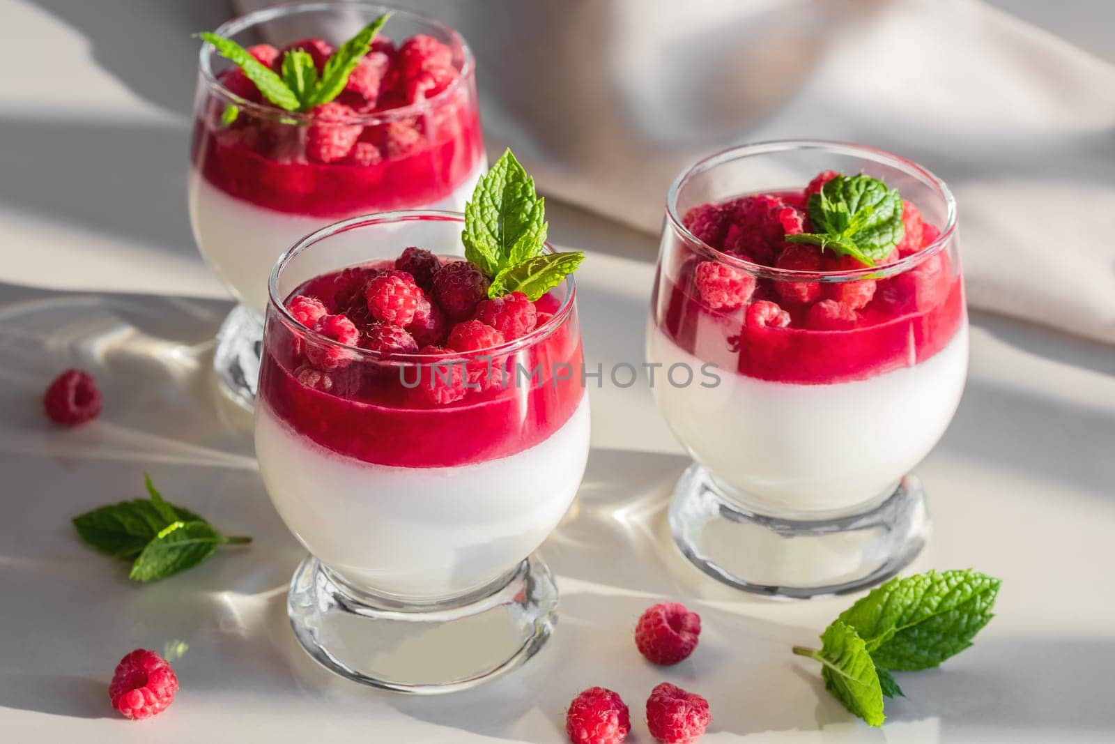 Panna cotta with raspberry jelly and mint leaves in glass glasses on a white table.