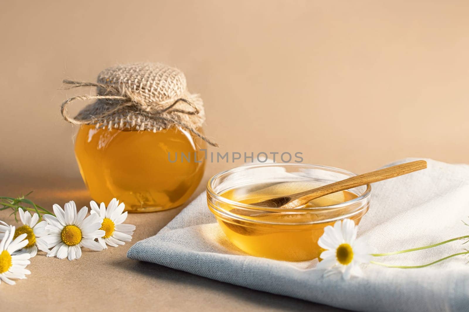 Chamomile syrup in a small bowl and in a jar and chamomile flowers on a linen kitchen towel, copy space by galsand